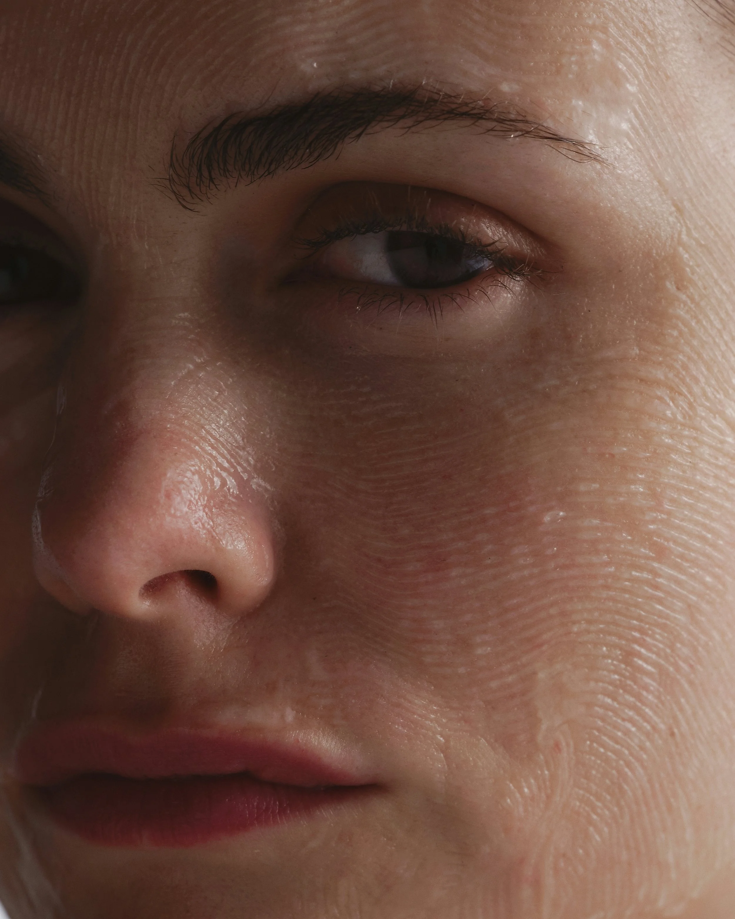 Close-up of a woman's face with smooth skin, full lips, and well-groomed eyebrows, illuminated by natural light.