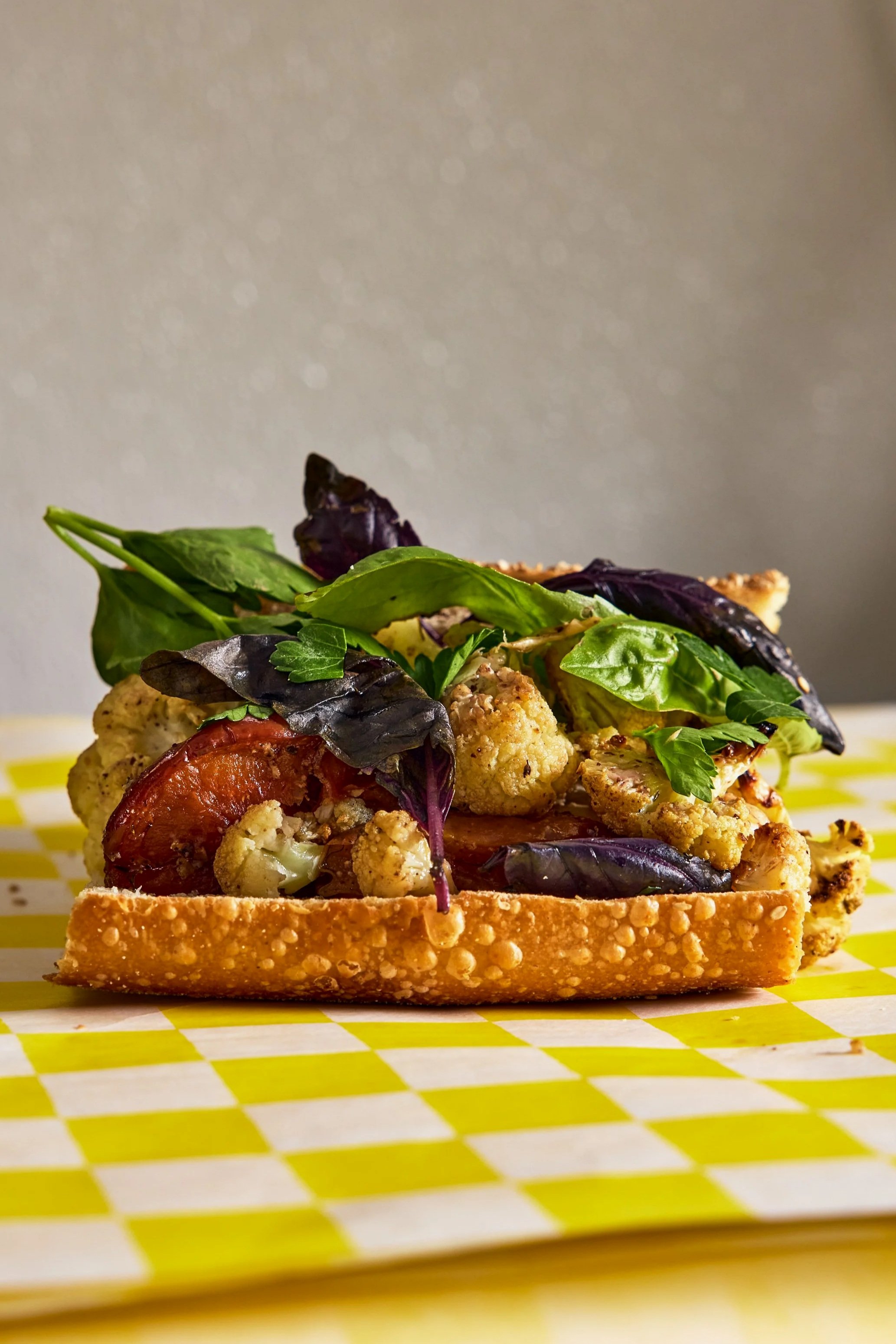 Jerry's hoagie sandwich with roasted cauliflower, tomato, and basil leaves on top of a toasted bun.