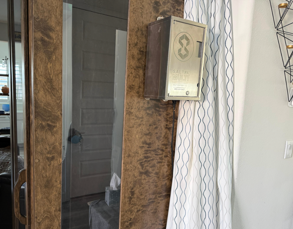 Metal electrical box mounted on a wall near a white curtain, with a tissue box on a small stand below it.