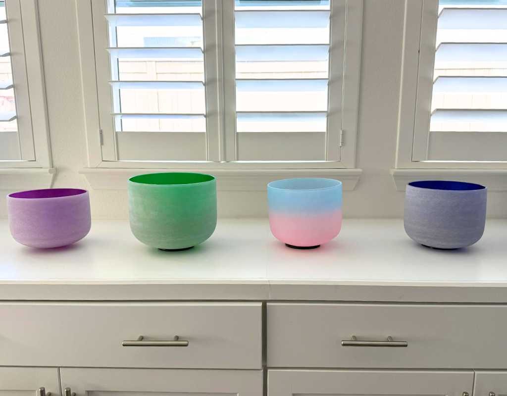 Four colorful flower pots on a white countertop in front of a window with white shutters.