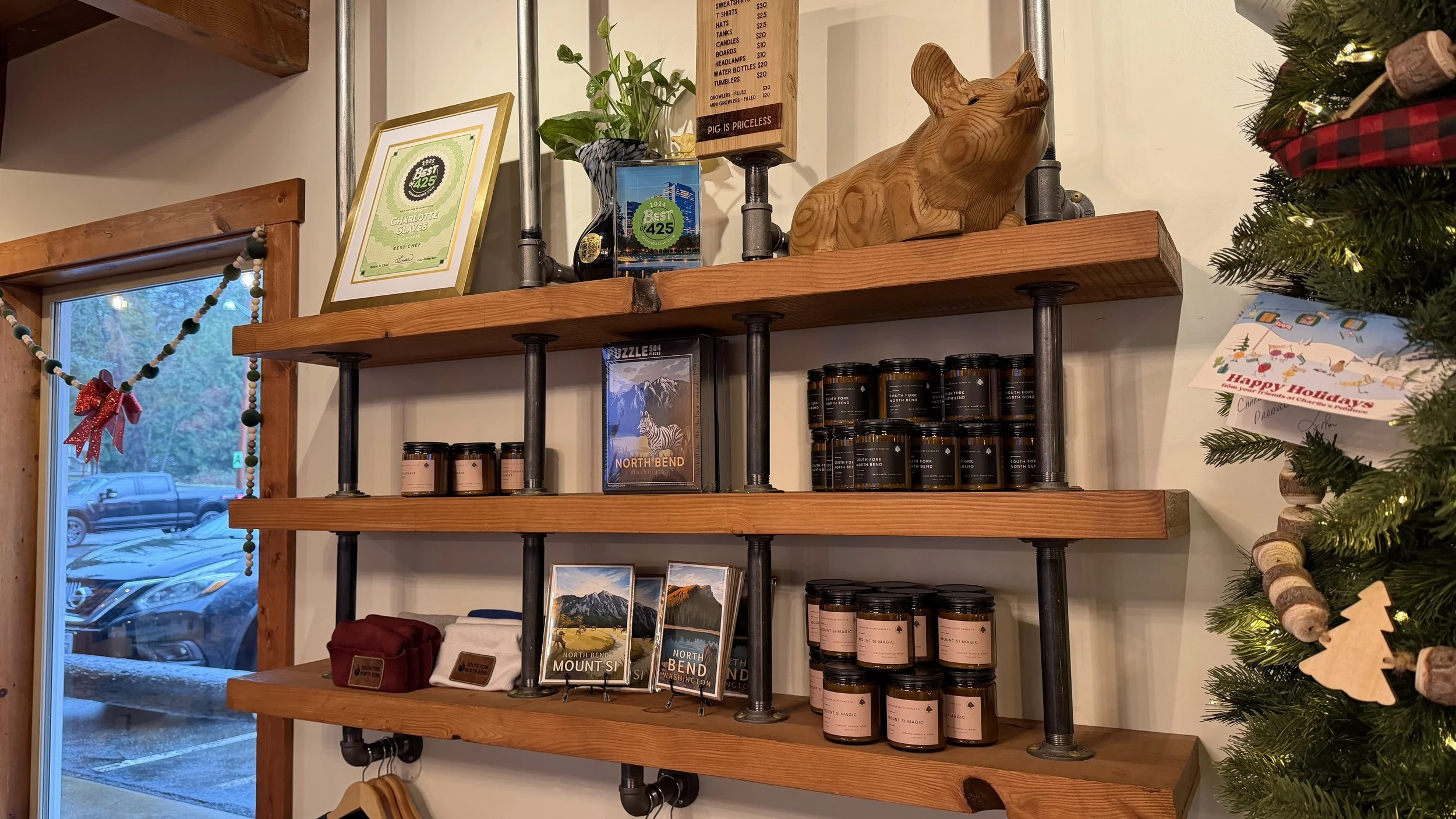 Wooden shelves with black pipe supports displaying framed pictures, jars, and a wooden pig sculpture. A window with holiday decorations and a Christmas tree with ornaments are also visible.