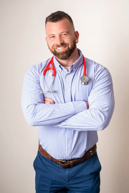 Male doctor smiling with arms crossed, wearing a stethoscope around his neck and a blue checkered shirt.