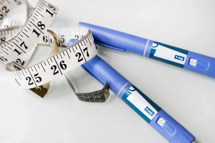 Two blue insulin pens with measuring tapes wrapped around them on a white surface.