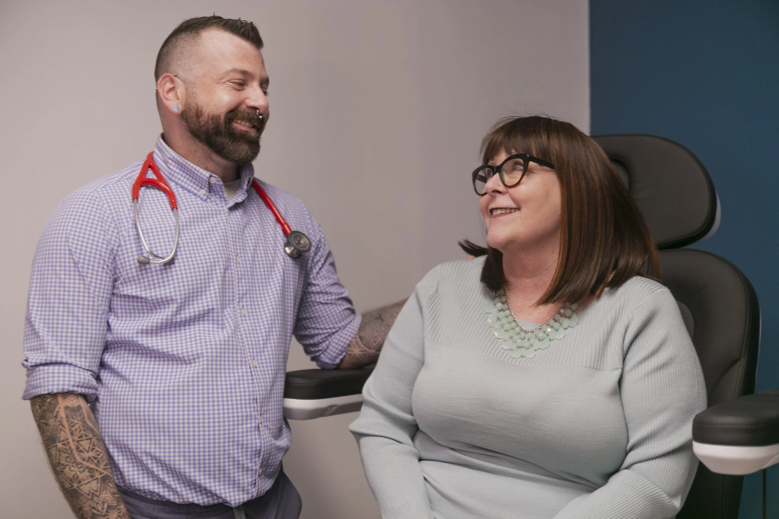 Primary care clinician speaking with an adult patient during a medical visit in a private office setting.