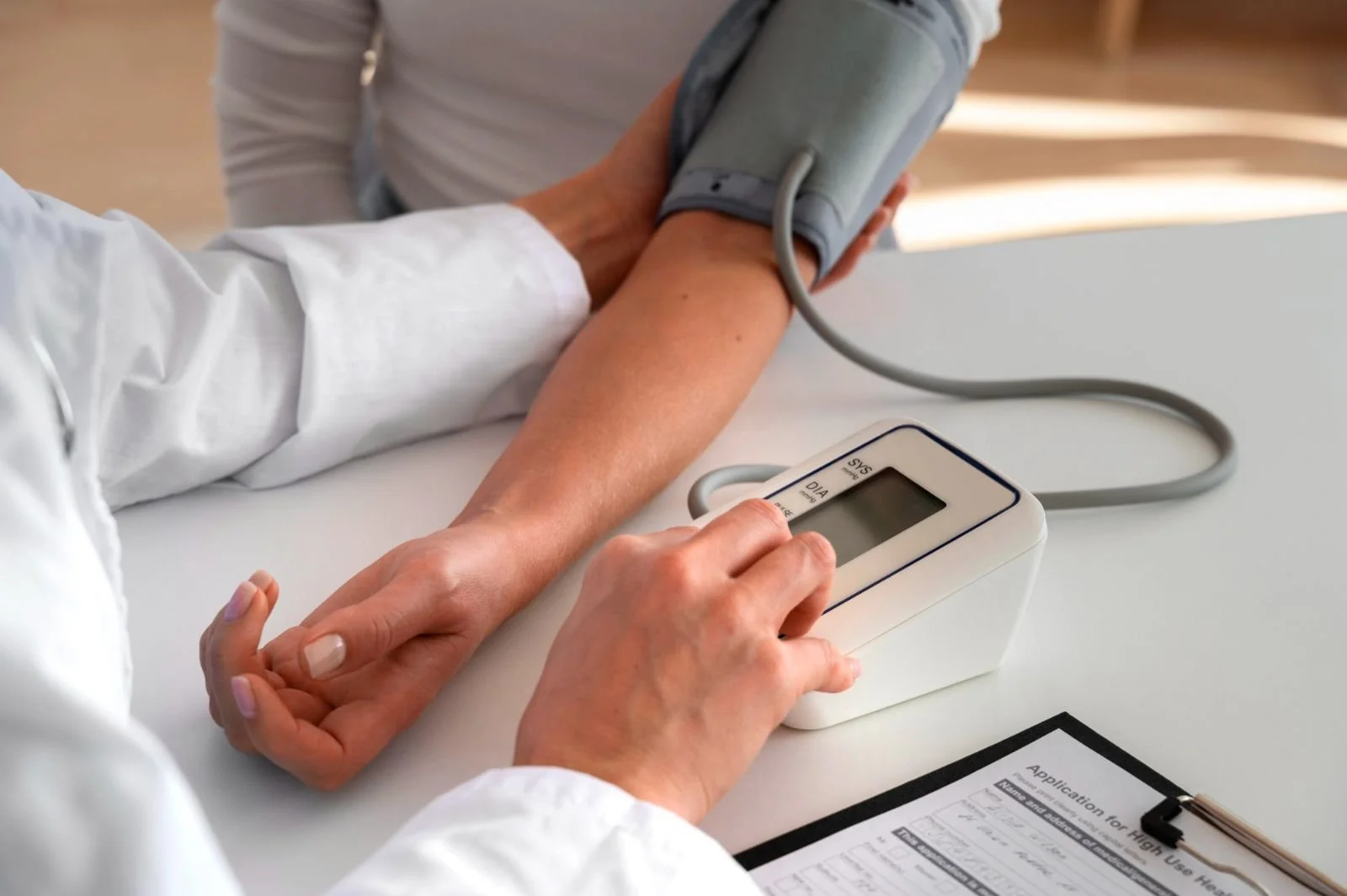 A healthcare professional measuring a patient's blood pressure using a sphygmomanometer and digital monitor at a medical setting.