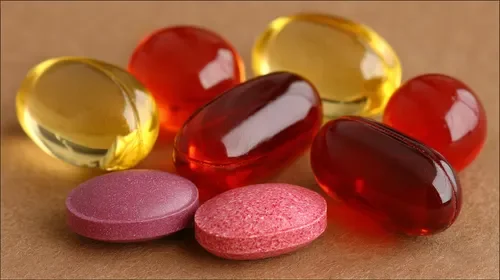 Assorted colorful softgel capsules and tablets on a brown background.