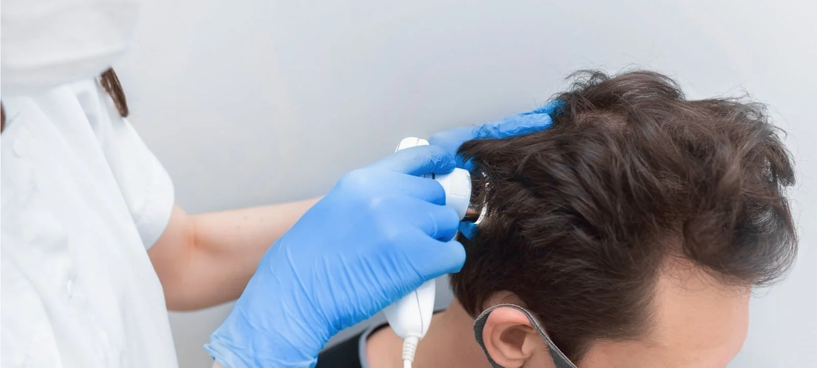 A healthcare professional in blue gloves performing an ear exam on a man with curly hair, wearing a face mask.