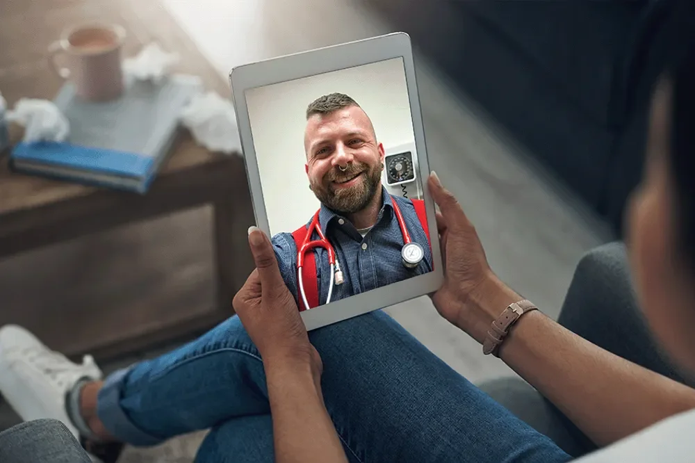 Person holding a tablet showing a smiling healthcare professional with a stethoscope around his neck.