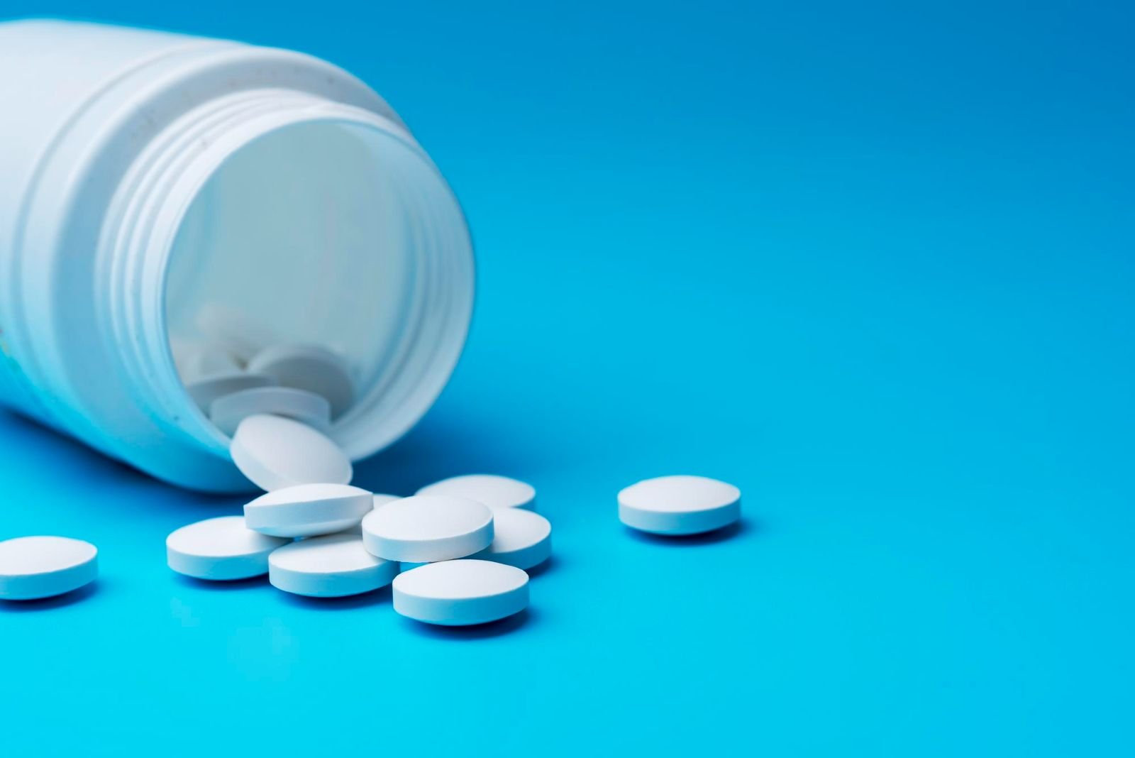 White tablets spilling from an overturned prescription bottle on a blue background.