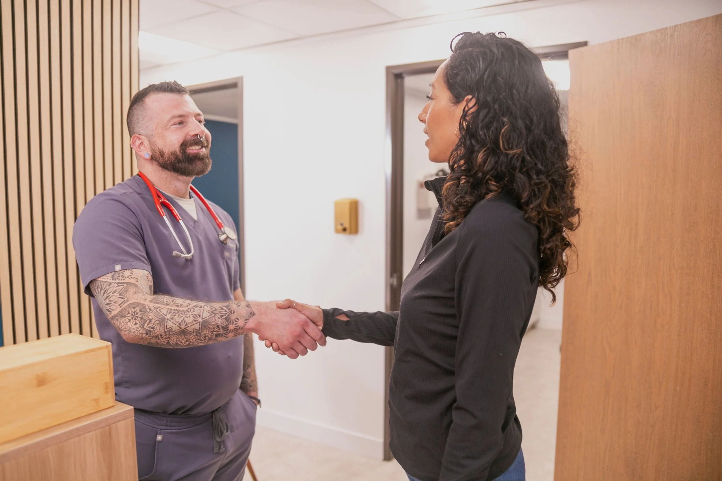 Primary care clinician welcoming an adult patient during a medical visit, reflecting patient-centered care in a modern clinic setting.