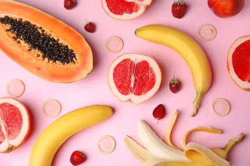 Assorted fresh fruits including papaya, grapefruit, banana, strawberries, and grapefruit slices on a pink background.