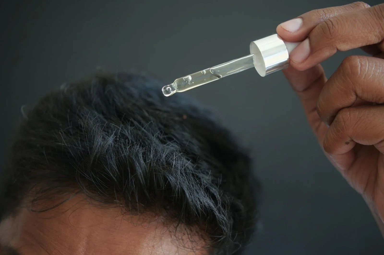 Hair Loss & PRP Treatments in Beverly Hills 21 Hand holding a dropper with a clear liquid over a person's dark hair.