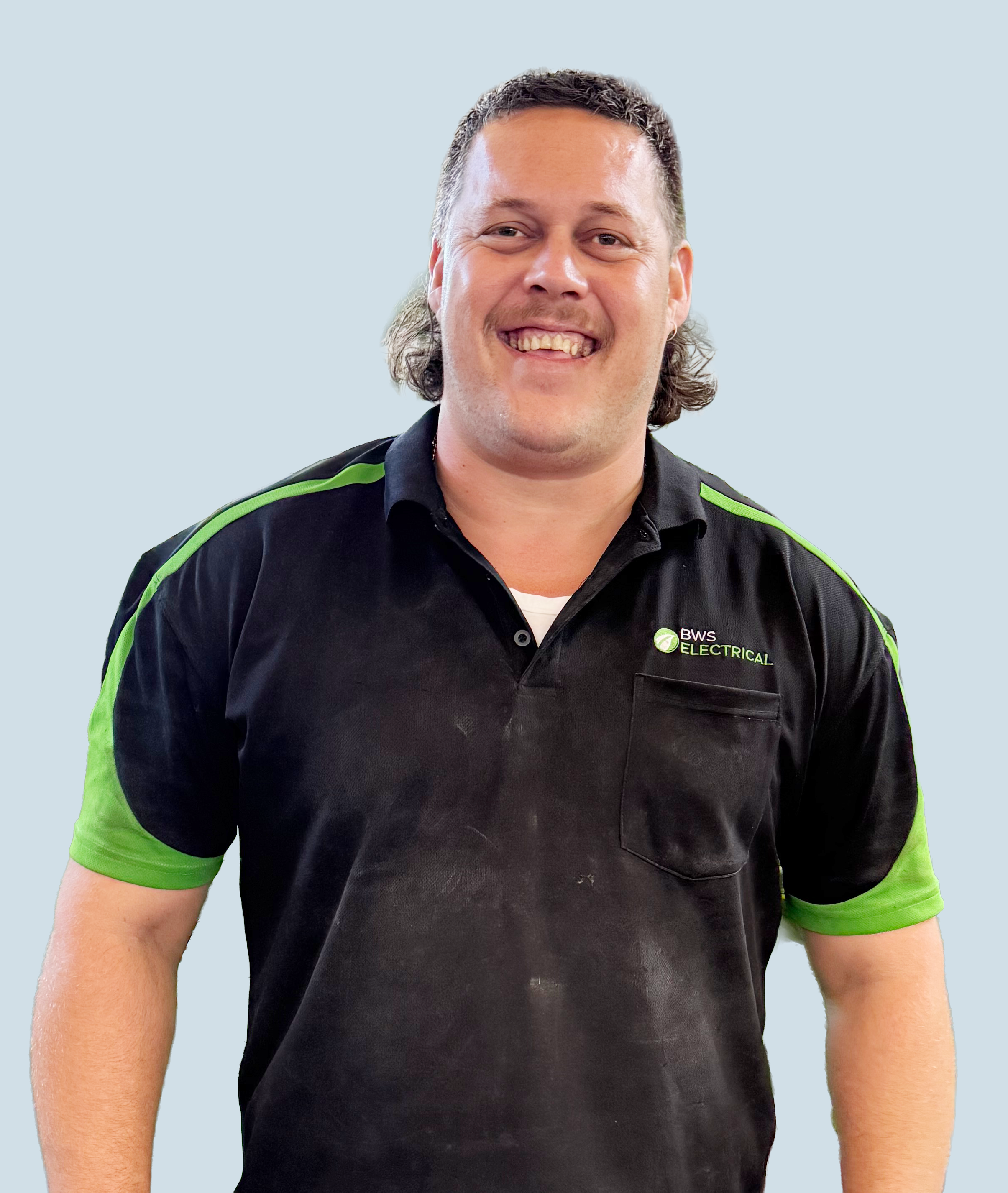 Man wearing a black and green work shirt with a logo that says 'BWS Electrical,' smiling against a light blue background.