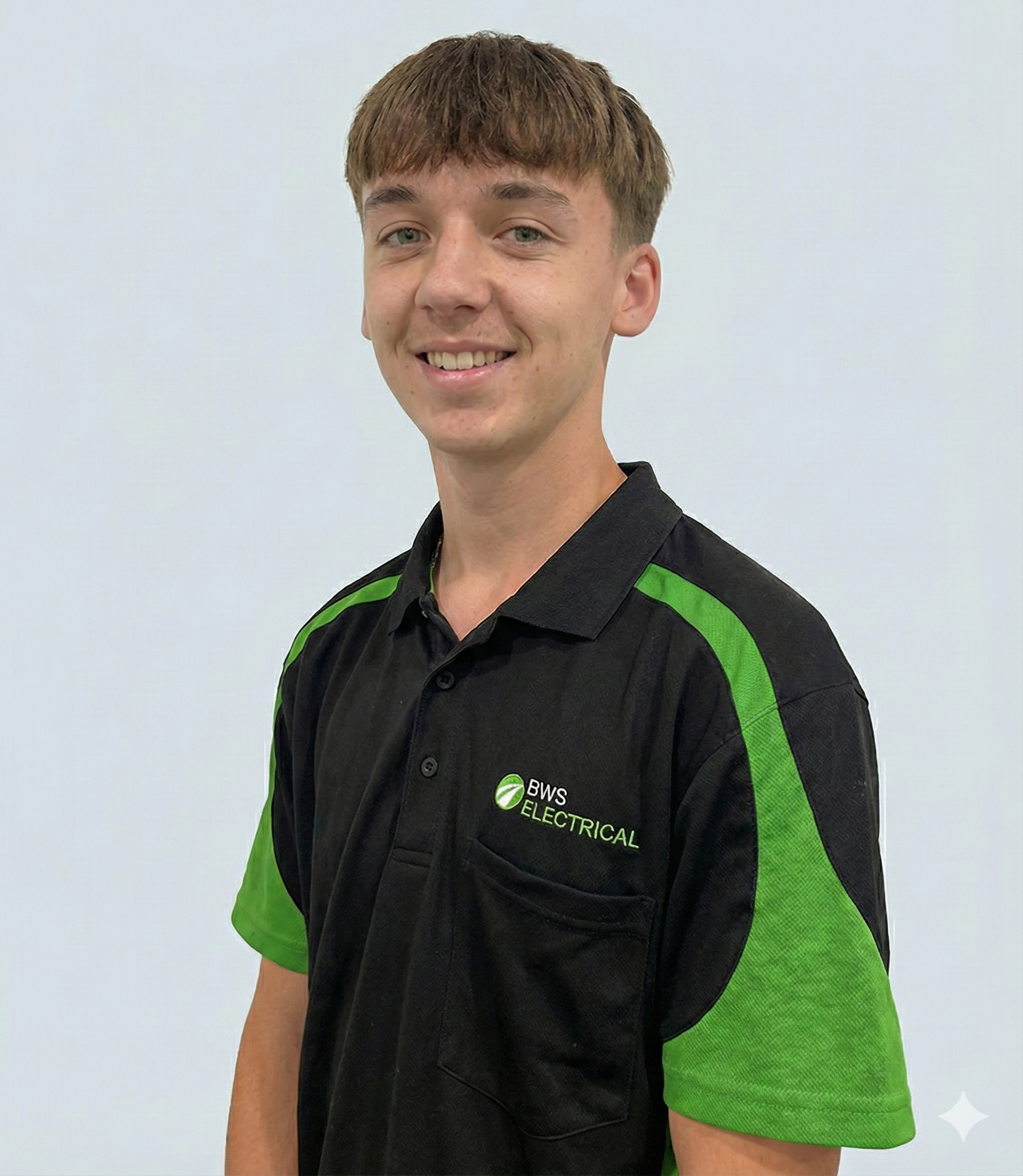 Young man with short brown hair smiling, wearing a black and green BWS Electrical polo shirt, standing against a plain light background.