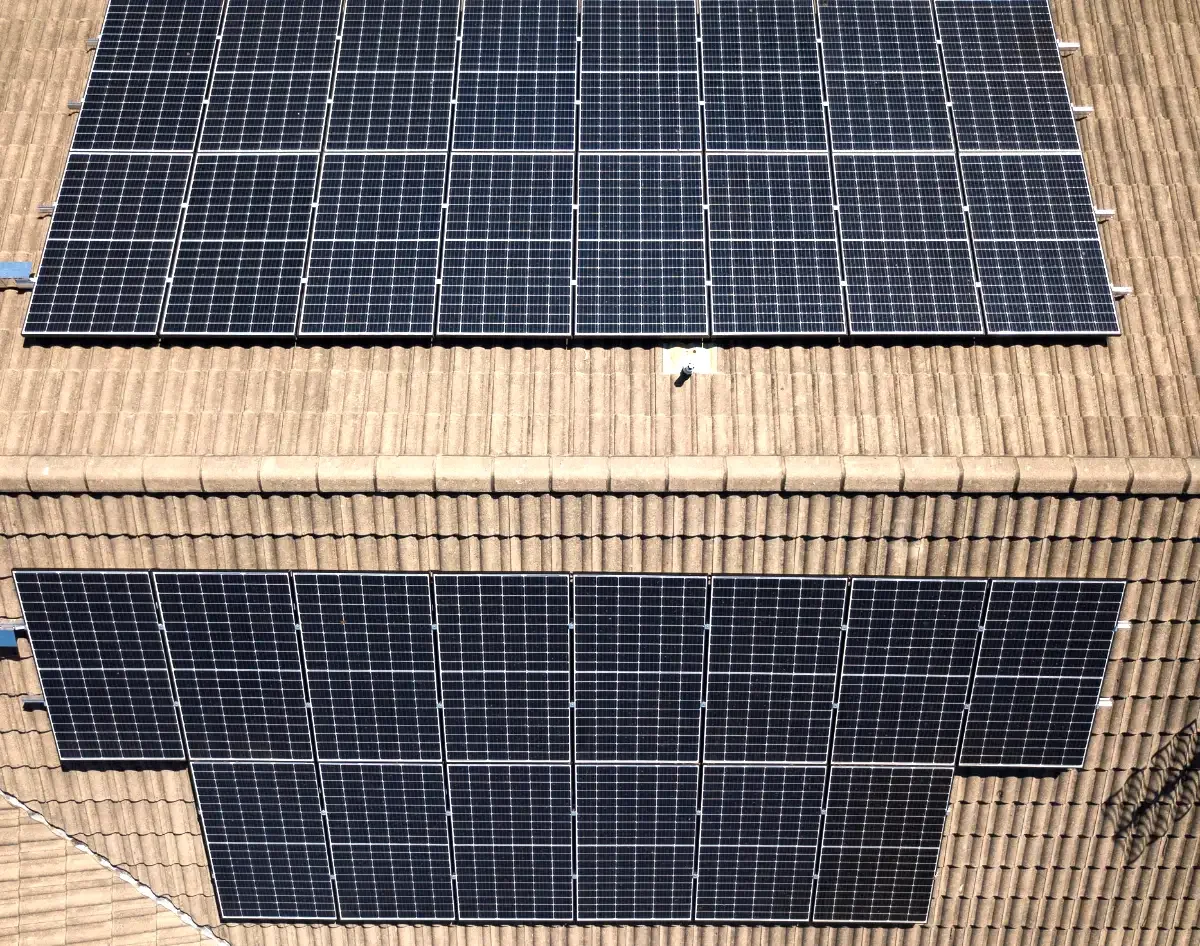 Aerial view of a roof with two sets of solar panels installed on reddish-brown roof tiles.