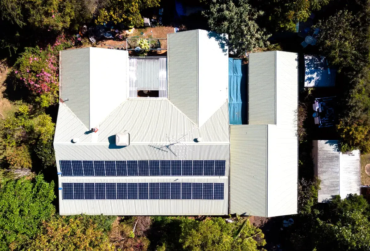 Aerial view of a house with solar panels on the roof, surrounded by trees and greenery.
