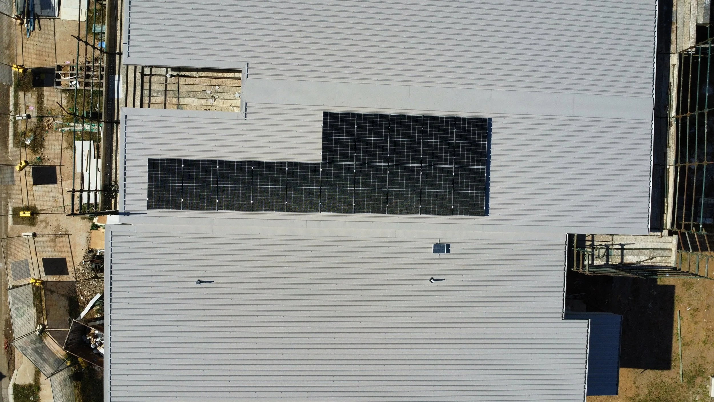 An aerial view of a building with a metal roof and solar panels installed on top.