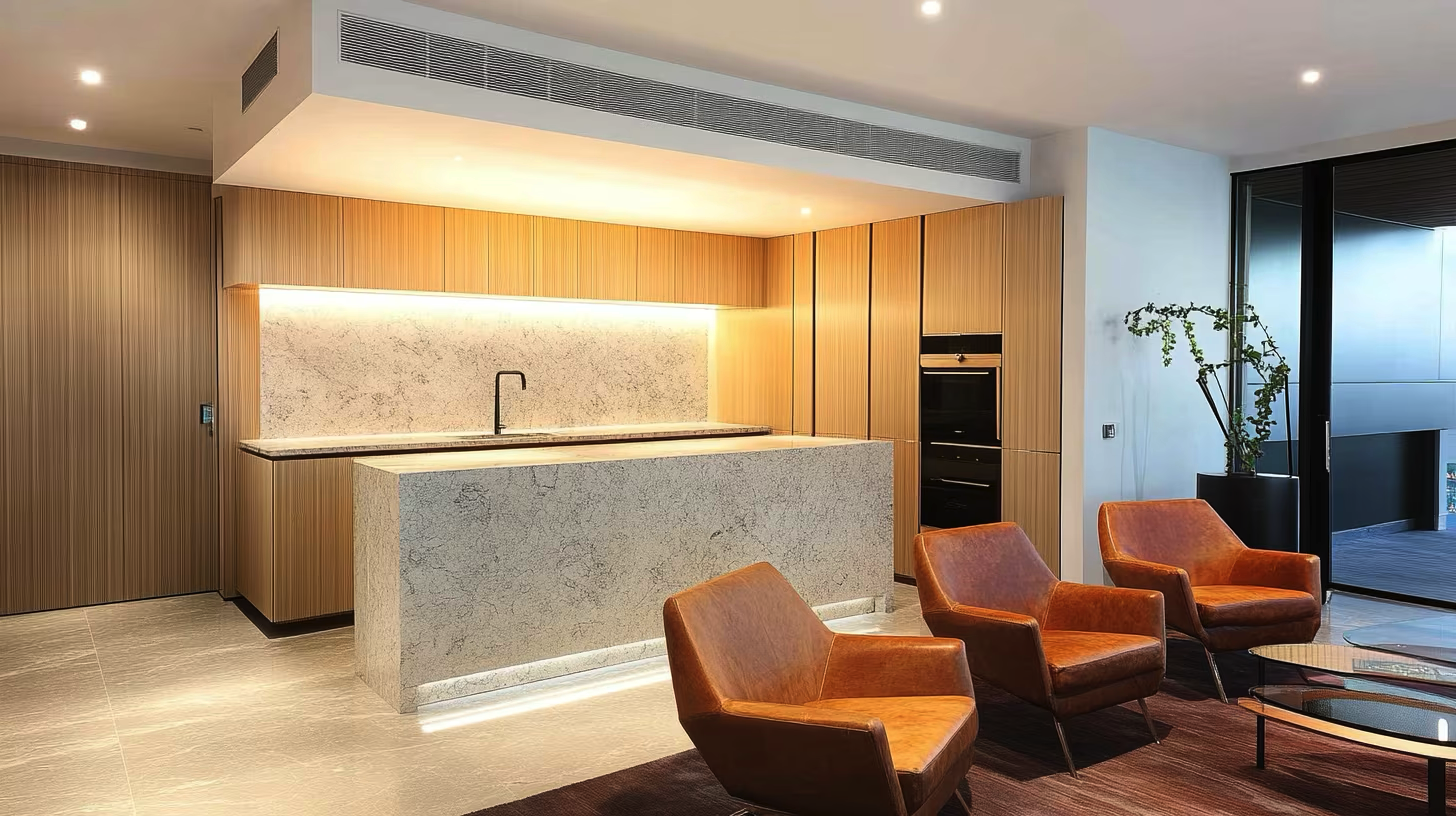 Modern kitchen with a marble island and wooden cabinets, and a seating area with three brown leather armchairs and a glass coffee table.