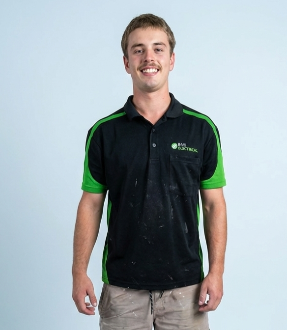 Young man wearing a black and green BNS Electrical polo shirt, standing against a plain light background, smiling at the camera.