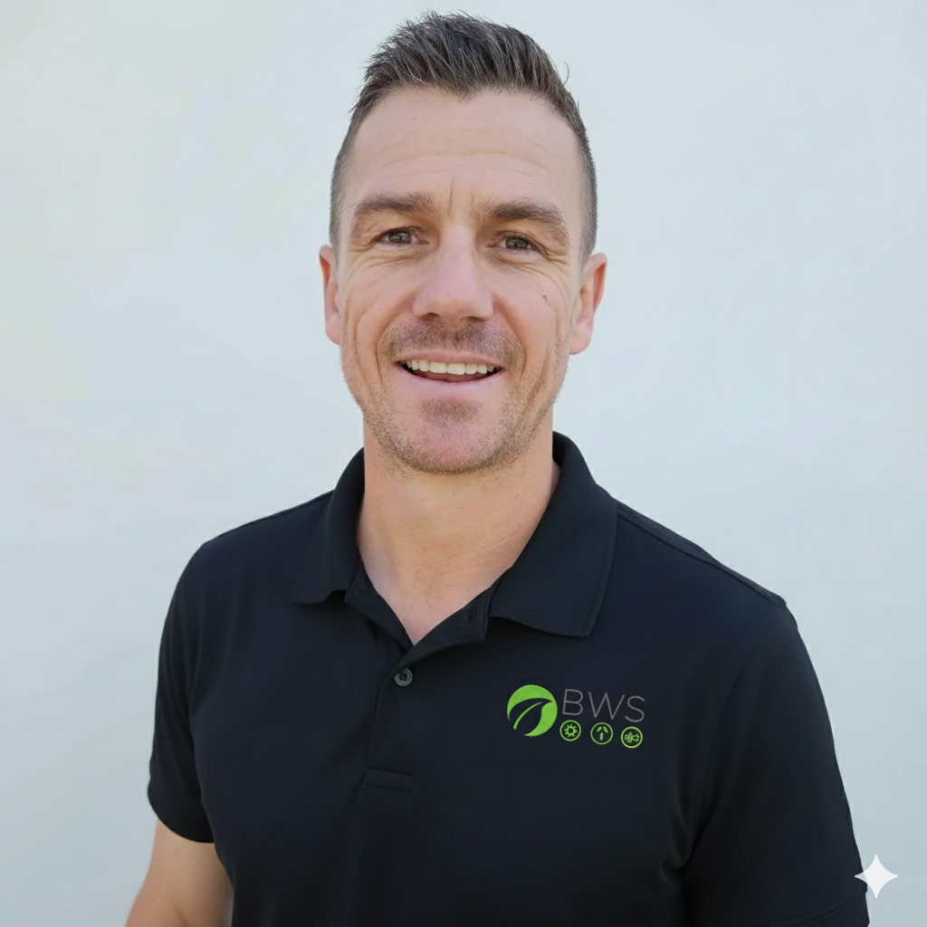 Smiling man with short dark hair wearing a black polo shirt with a BWS logo on the left chest, standing against a plain white background.