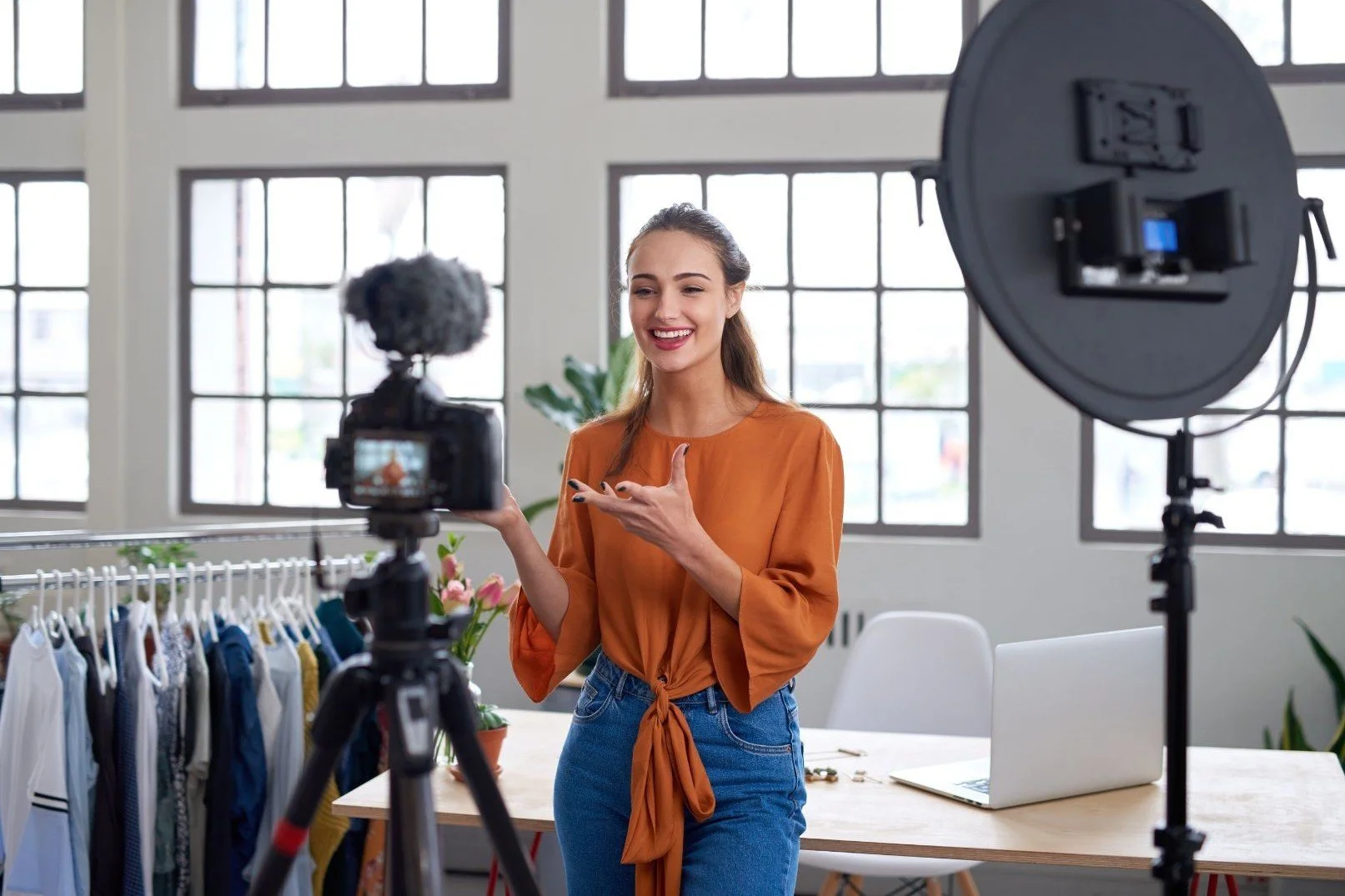 Fashion influencer filming social media video near a clothing rack, demonstrating professional content creation and organized campaign coordination for retail brands.