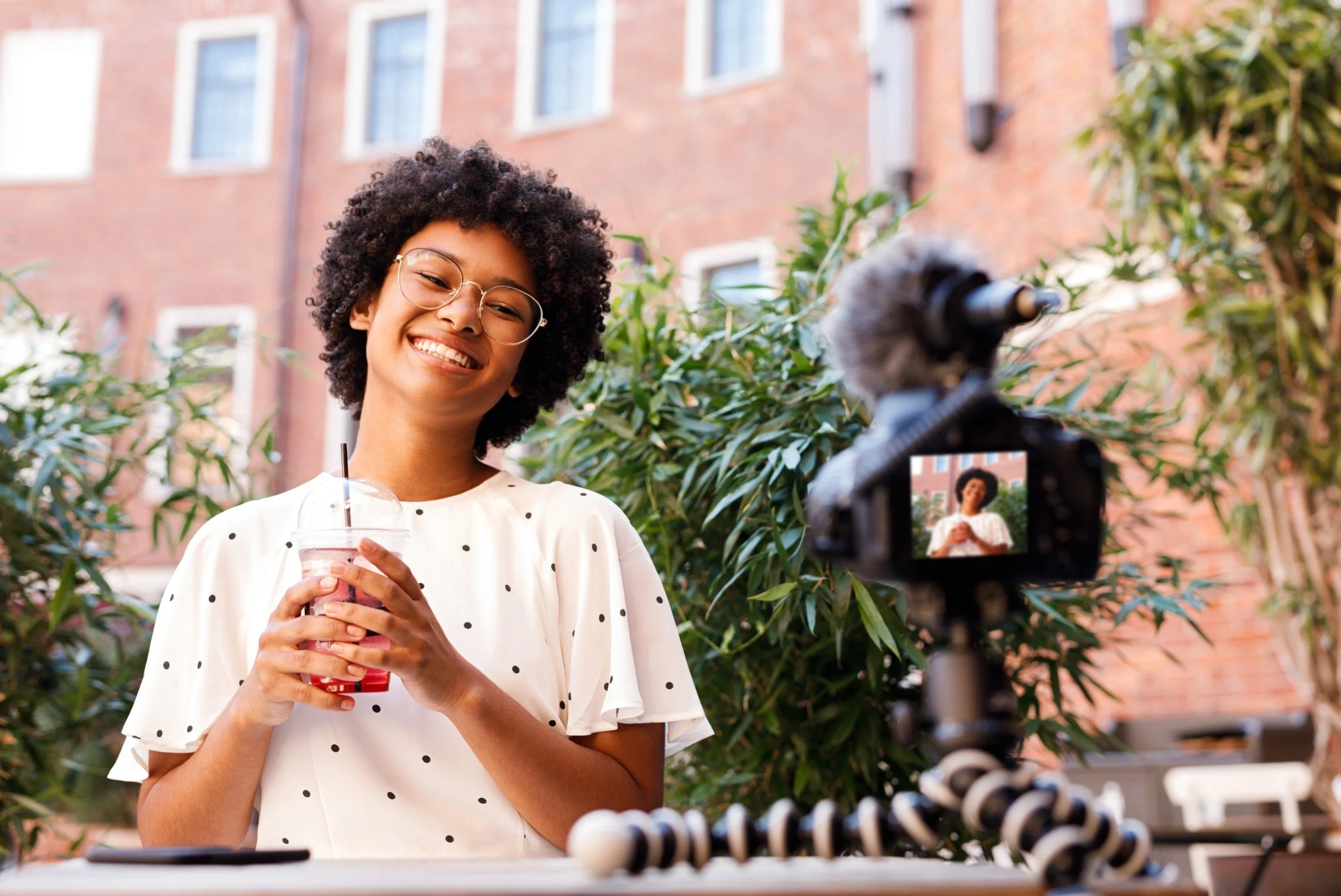 A young female influencer smiling at a camera mounted on a tripod while filming content outdoors, representing influencer marketing, content creation, and the importance of evaluating creator performance metrics before partnership.