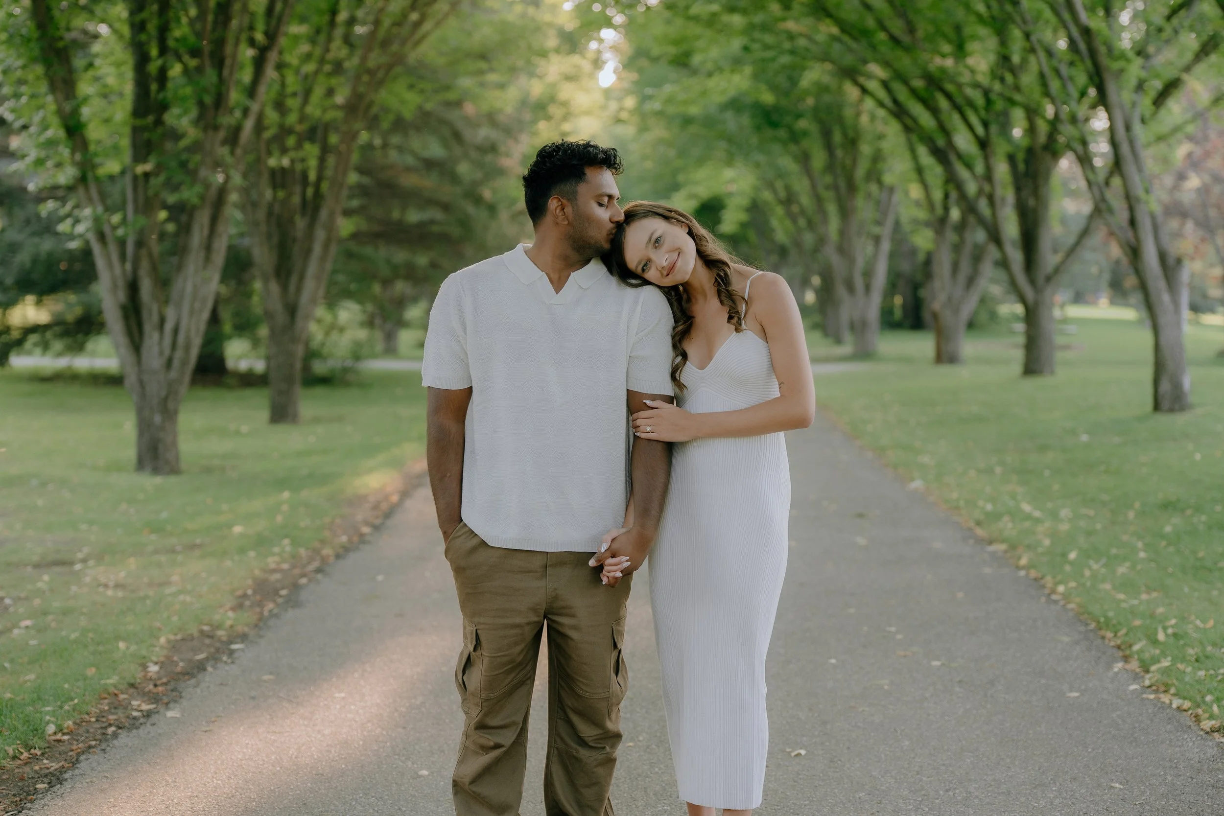 A couple walking hand in hand on a tree-lined path, with the woman leaning her head on the man's shoulder
