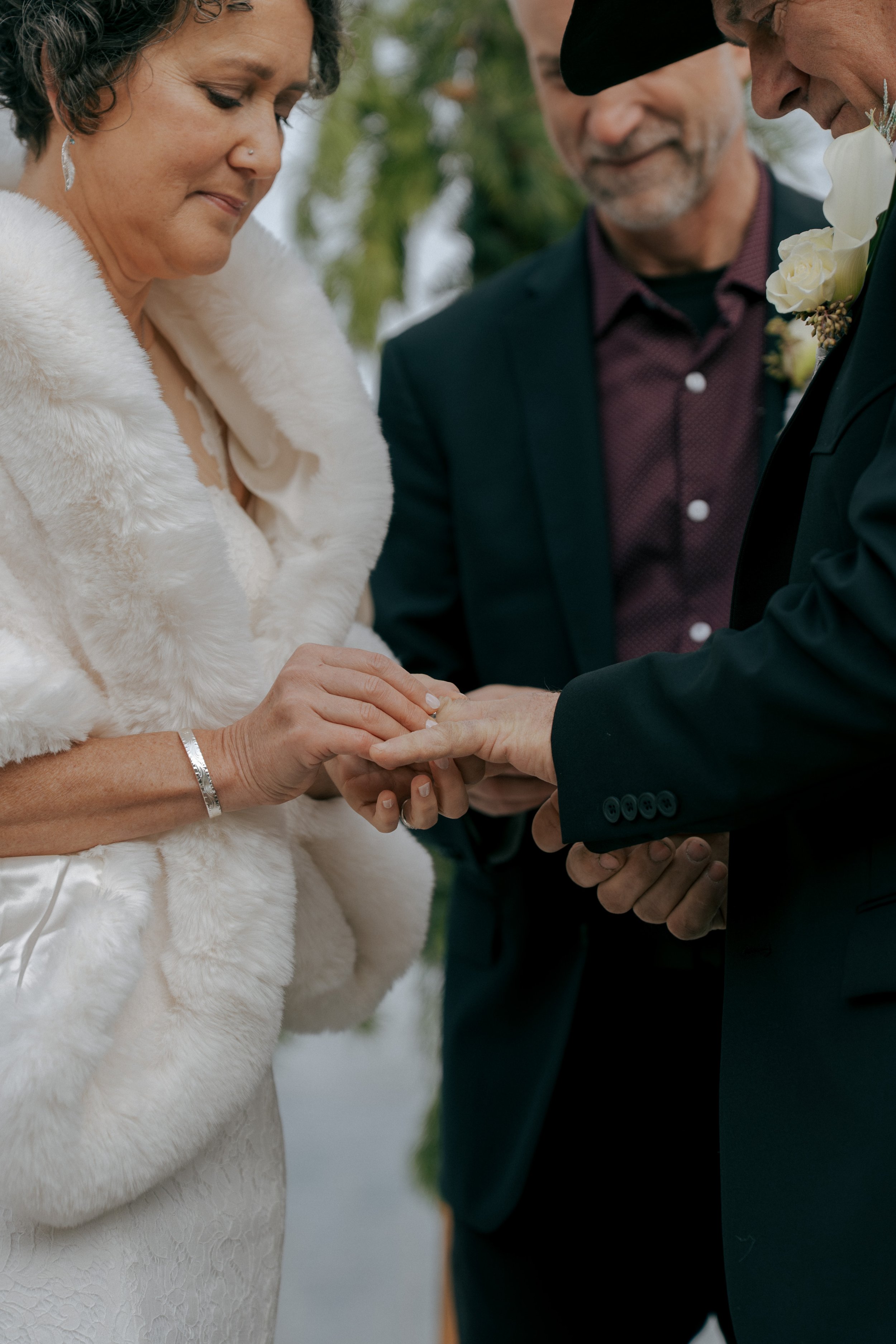 A couple getting married outdoors, exchanging rings with an officiant standing close by, officiating their wedding ceremony.