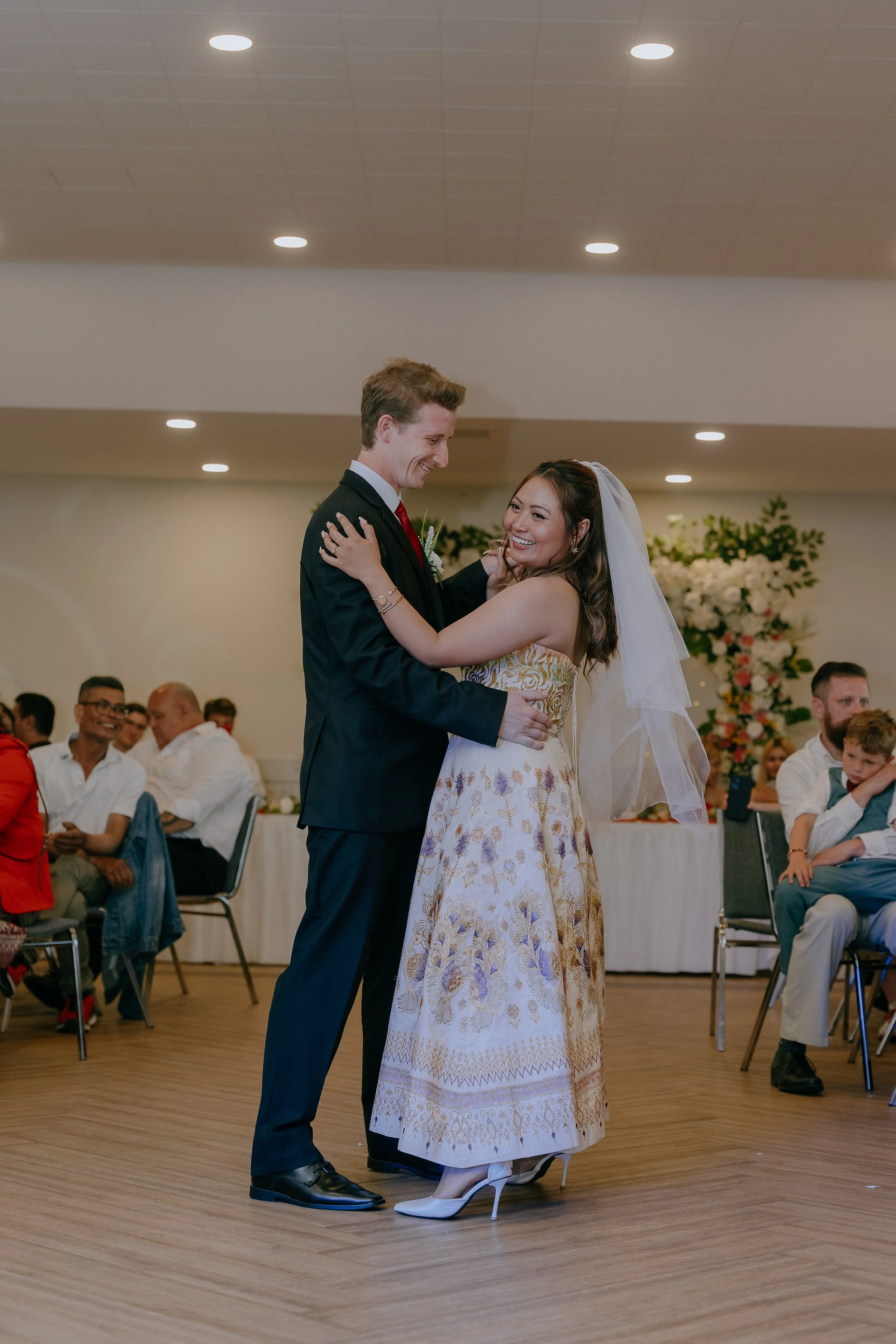 A bride and groom dance at their wedding reception, surrounded by seated guests.