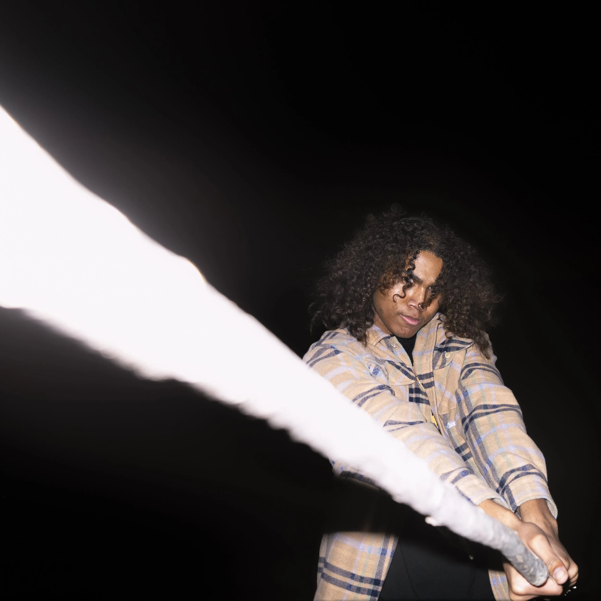 A woman with curly hair, wearing a plaid shirt, pulling a thick rope with a determined expression against a black background.