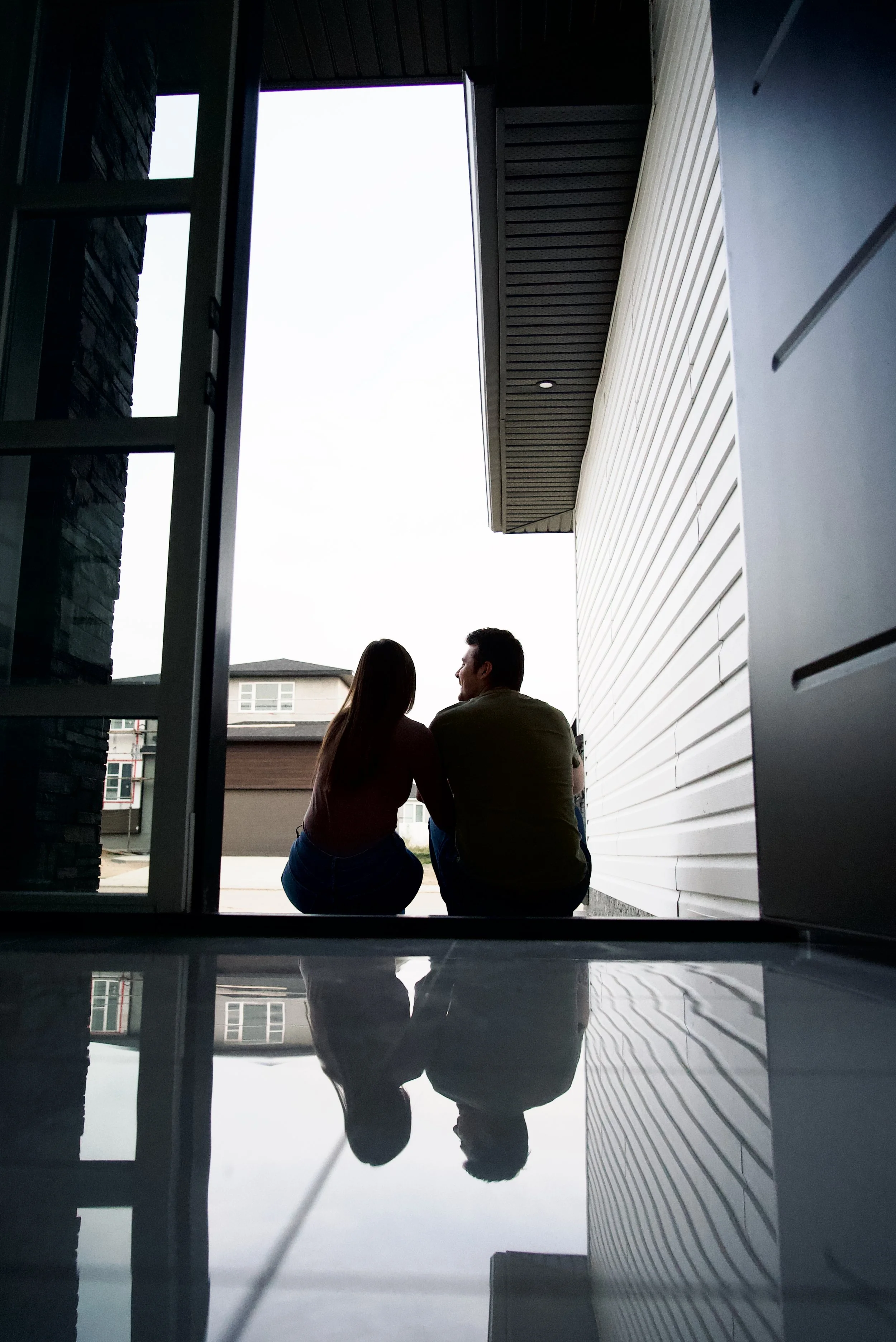A silhouette of a couple sitting outdoors, facing each other and engaging in conversation, with their reflections visible on the floor.
