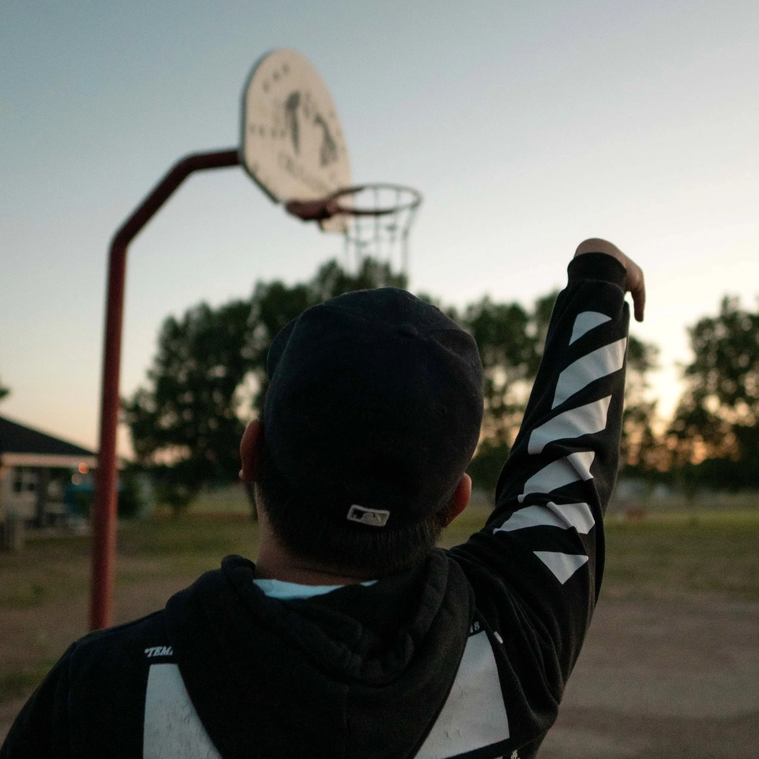 Person shooting basketball on an outdoor court during sunset.