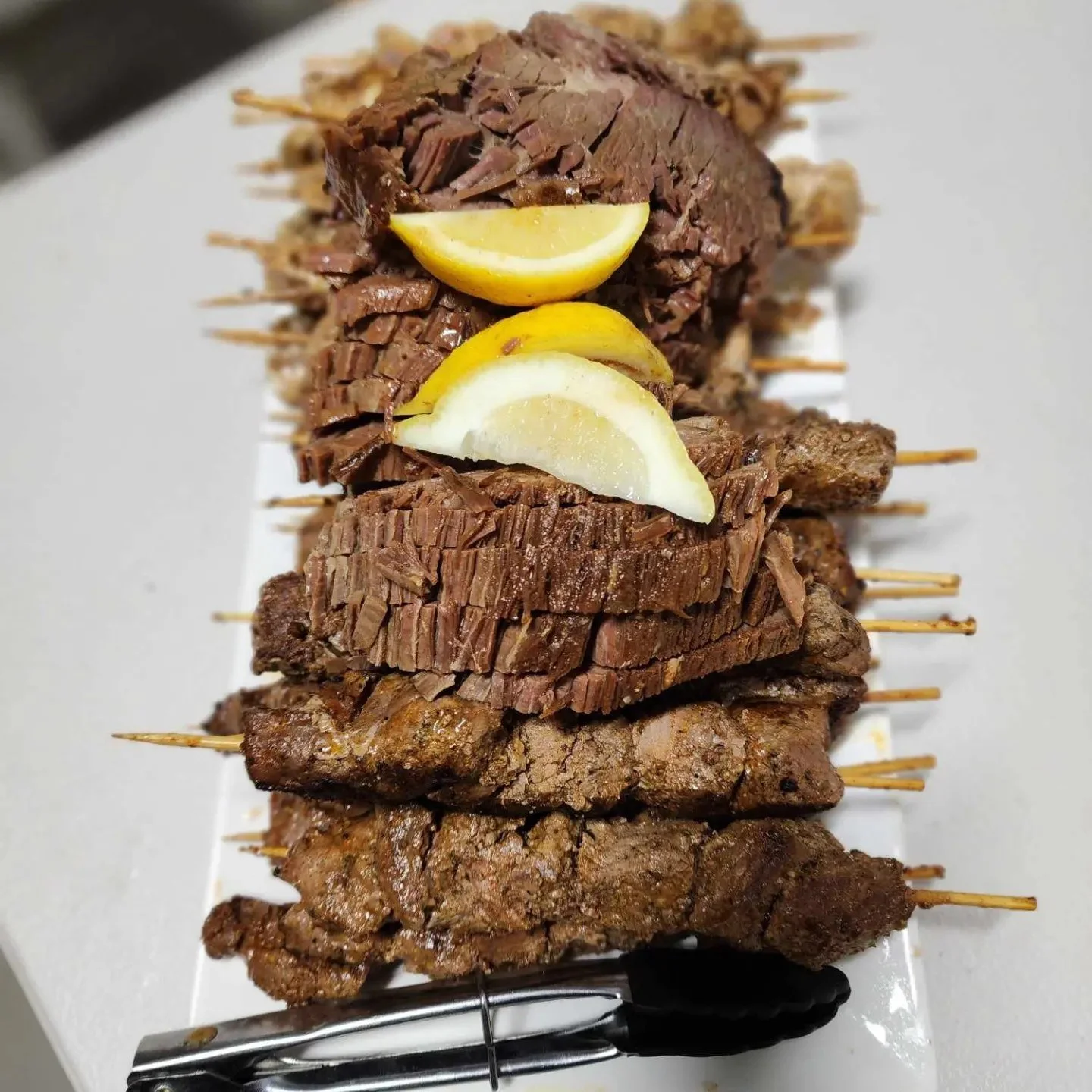 Skewers of grilled meat with lemon wedges on a white tray.
