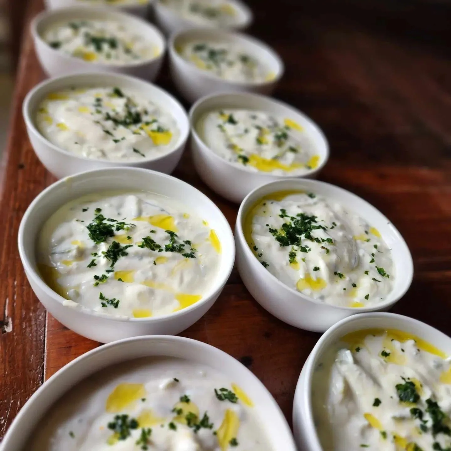 Bowls of raita, a yogurt-based dish garnished with chopped herbs and a drizzle of oil, arranged on a wooden surface.