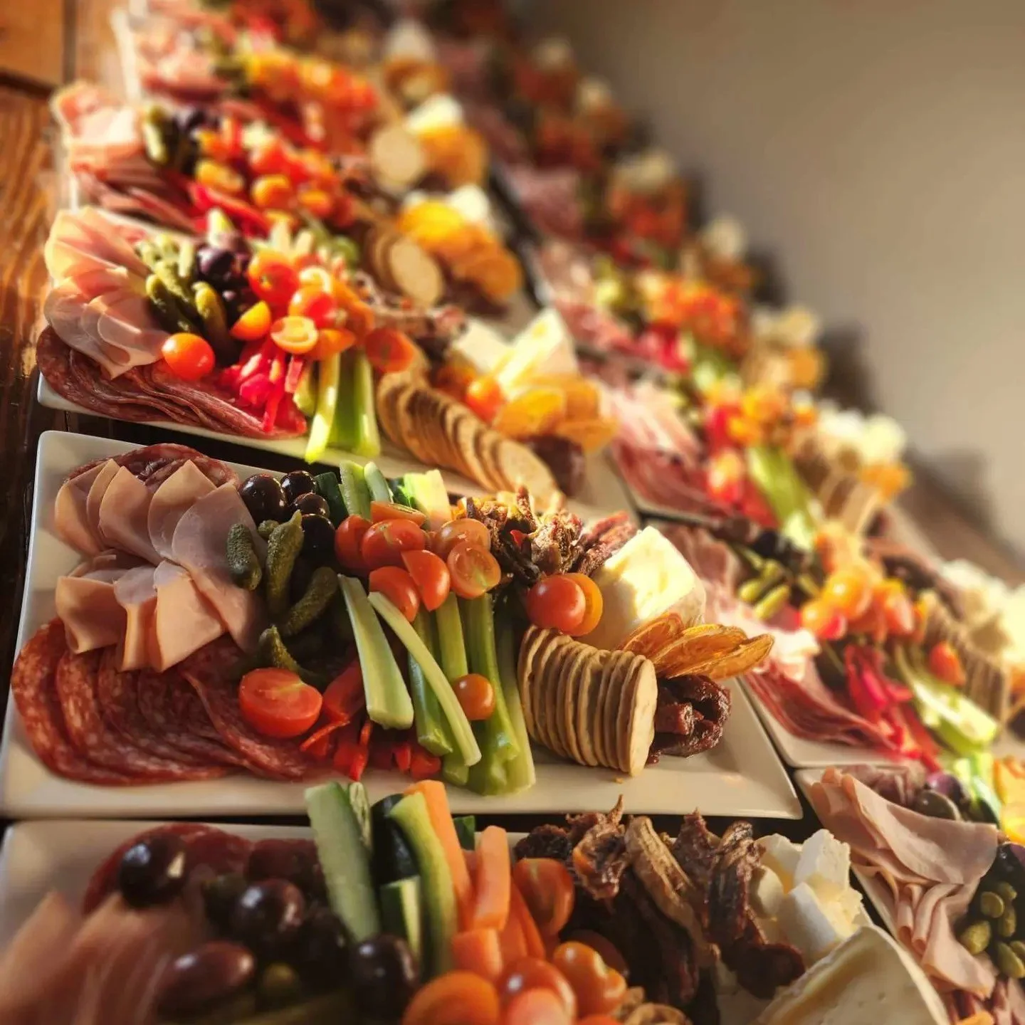 Variety of charcuterie boards with meats, cheeses, vegetables, and crackers arranged on white serving platters.