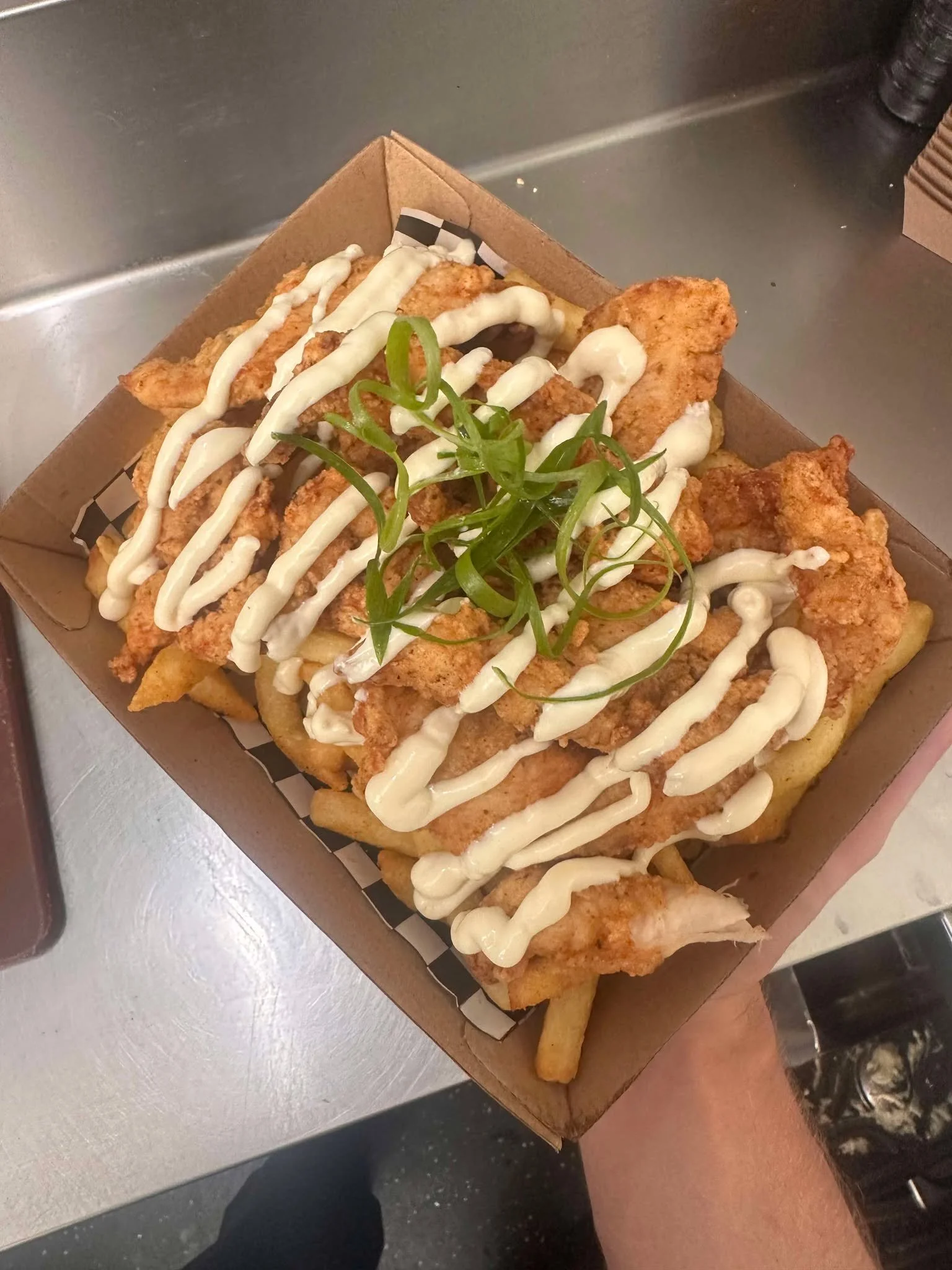 Fried fish fillets with tartar sauce on top, served with French fries and garnished with green herbs in a takeout box.