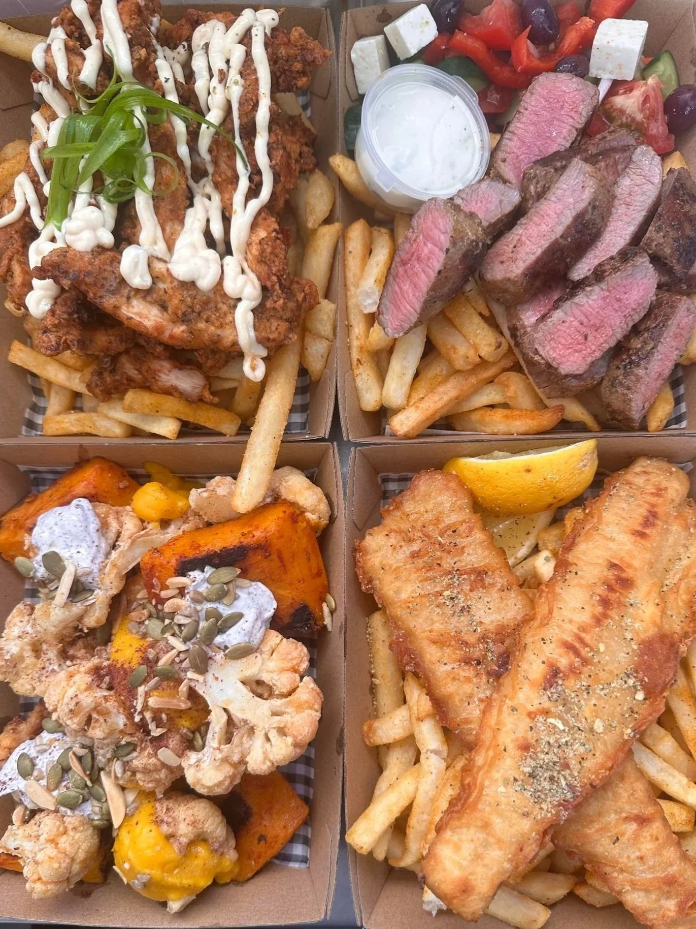 Four takeaway boxes filled with fried chicken, steak, fish, fried cauliflower and sweet potato, with French fries, dipping sauce, salad, lemon wedge, and garnishes.