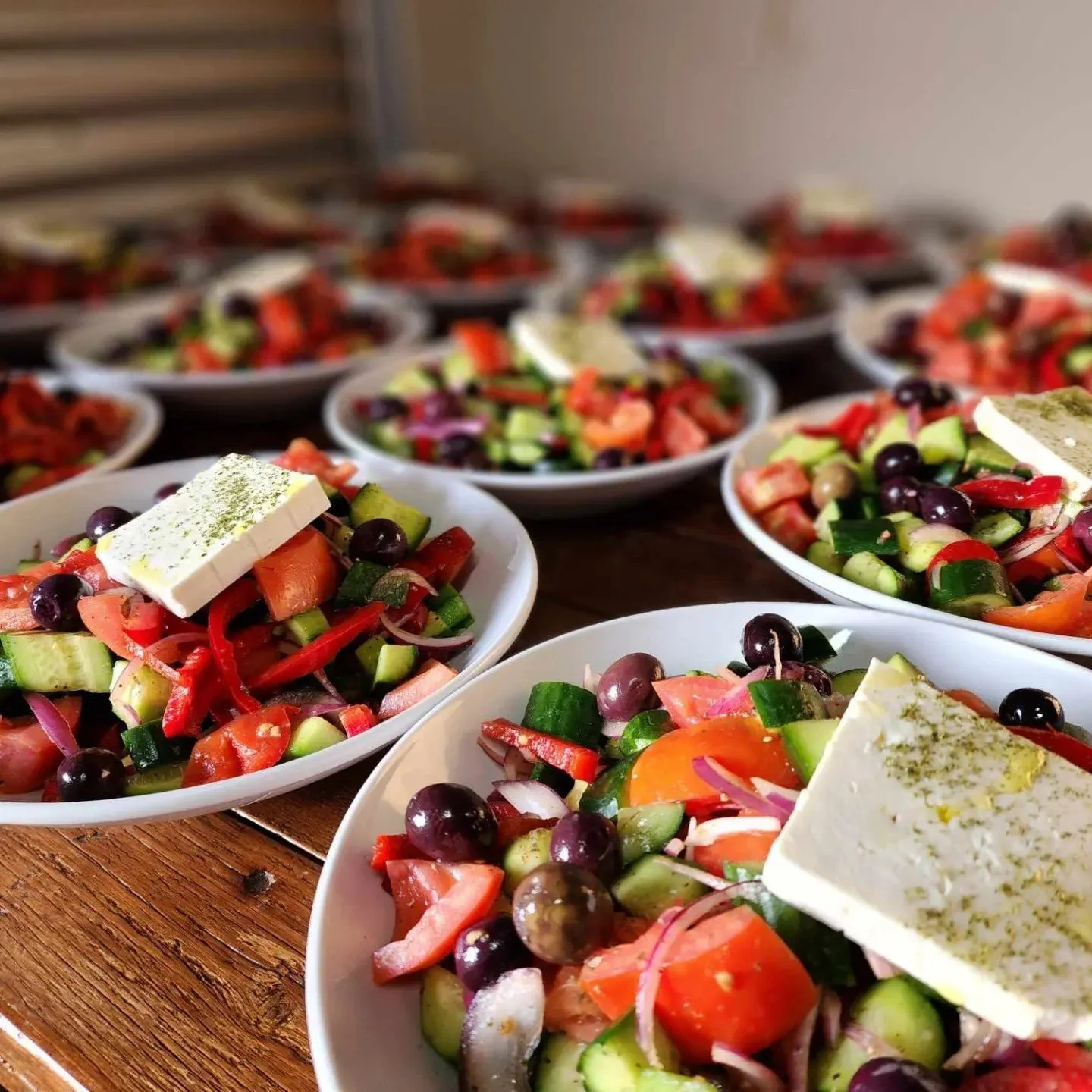 Several plates of fresh vegetable salads topped with slices of feta cheese on a wooden table.