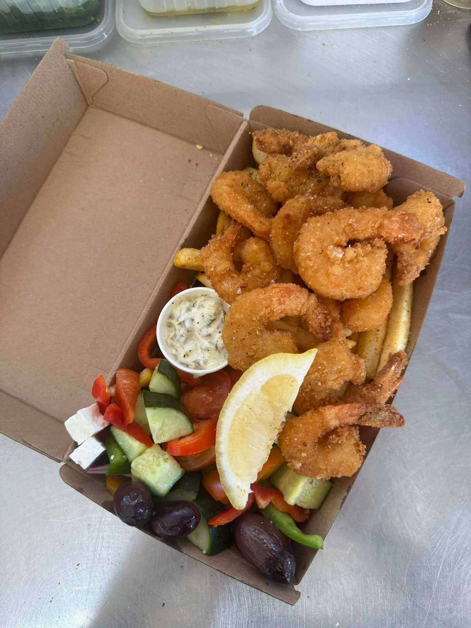 Fried shrimp with lemon wedge, side salad with chopped vegetables and feta, creamy dipping sauce, French fries in a takeout box.