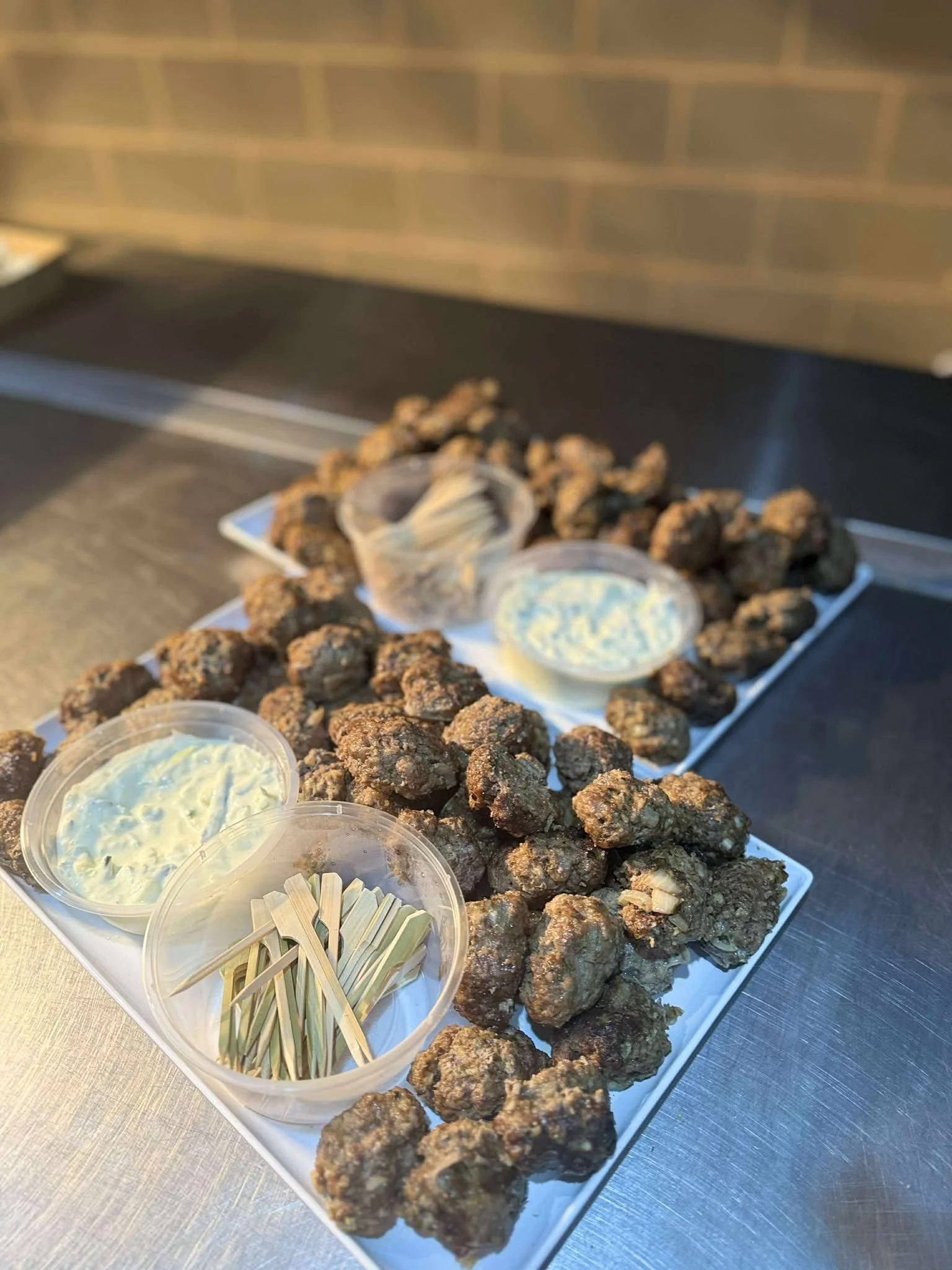 A white tray filled with fried chicken bites, lemon wedges, and small containers of ranch and other dipping sauces. The background features a brick wall and a black counter.