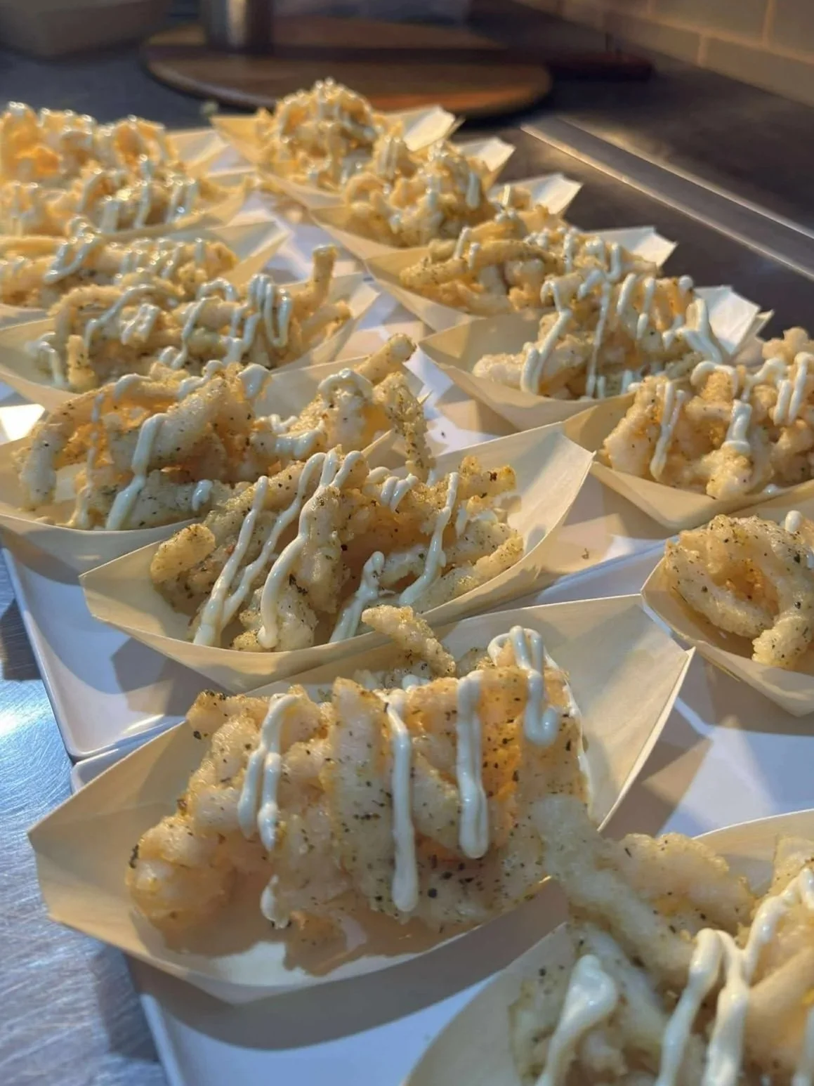 Crispy fried calamari served in small paper boats, topped with a drizzle of white sauce.