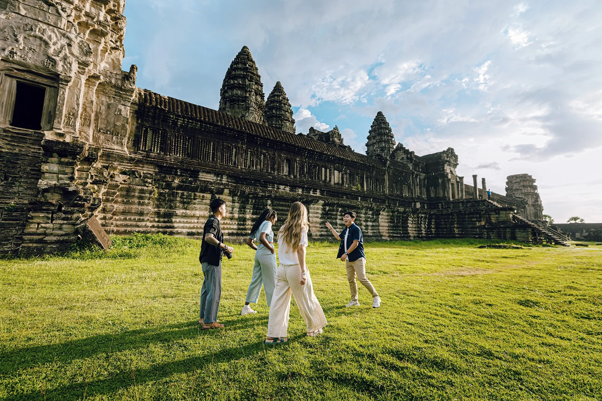 Group of five people standing on grass in front of ancient stone temple with towers, under a partly cloudy sky.