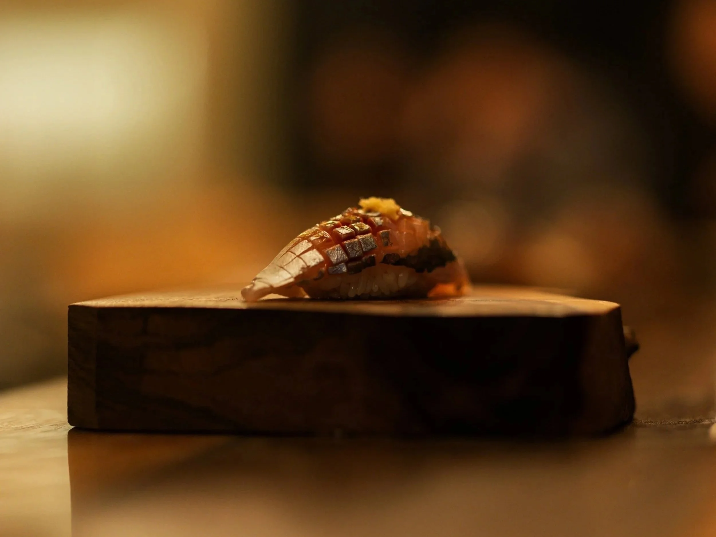 Close-up of a single piece of sushi on a wooden board with blurred background.
