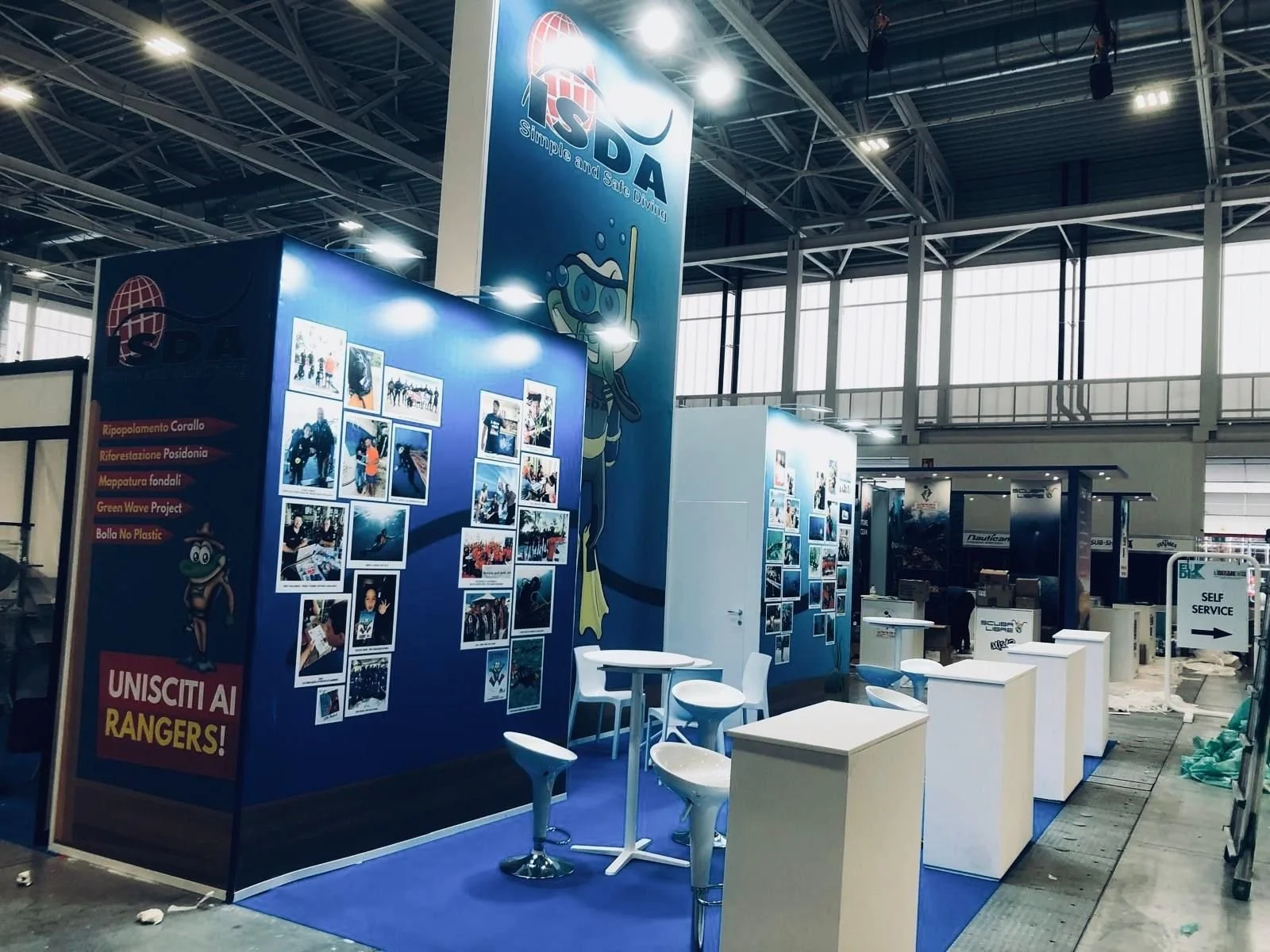 Stand espositivo con immagini di immersioni subacquee e un personaggio cartone animato con occhiali da sub, in un luogo come una fiera o esposizione.