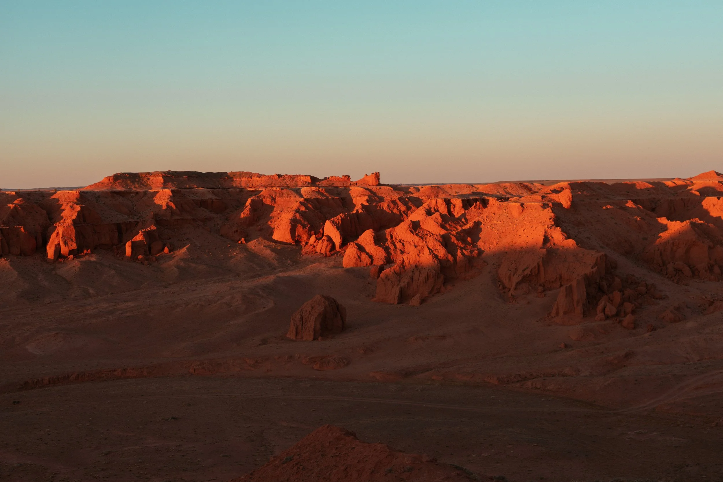 Sunset over a desert landscape with reddish rock formations and a clear sky.