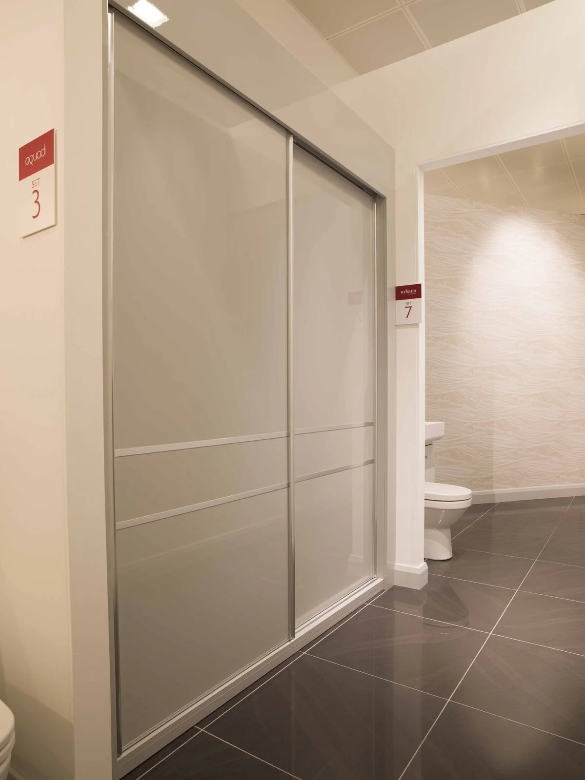 Modern bathroom with tiled floor, a toilet, a shower with sliding doors, and red directional signs on the walls.