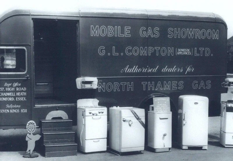 A mobile gas showroom van with display appliances and a small cartoon character cutout in front.