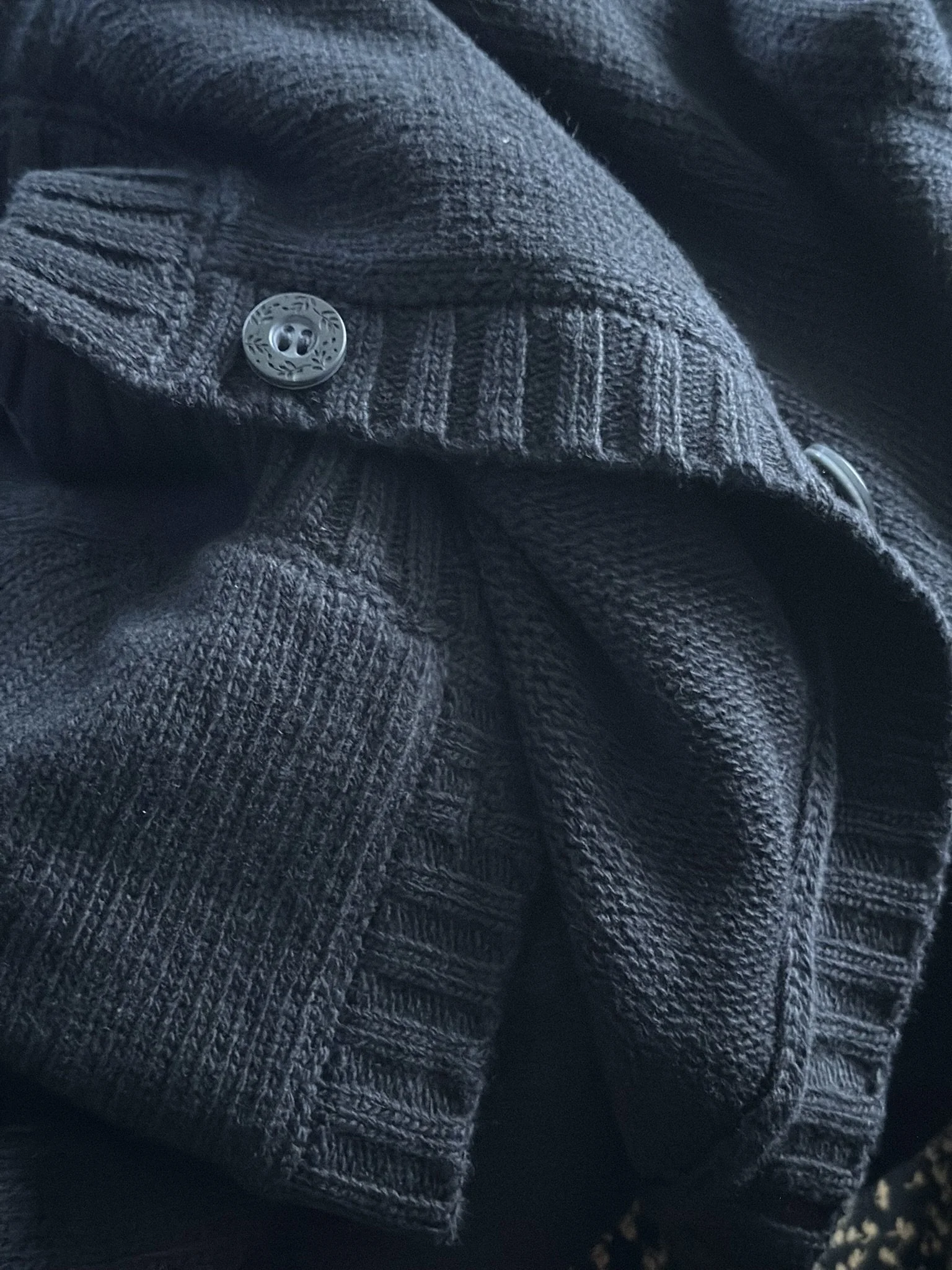 Close-up of a beige and black striped wool coat with a visible button on the sleeve.