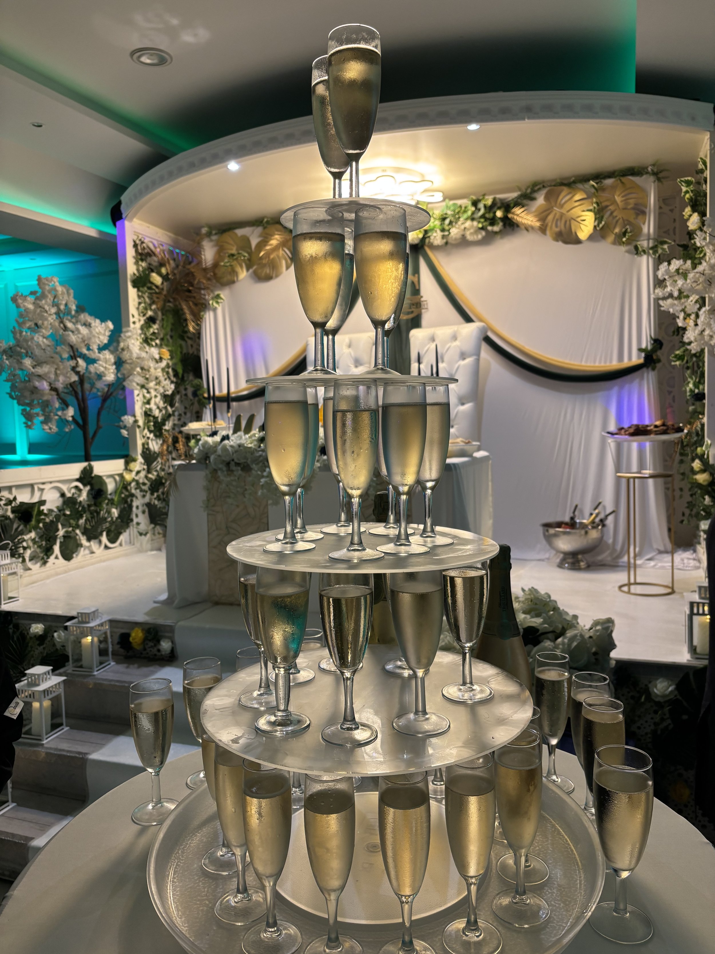 Gâteau de champagne en forme de pyramide dans un décor de mariage avec fleurs blanches et settings élégants.