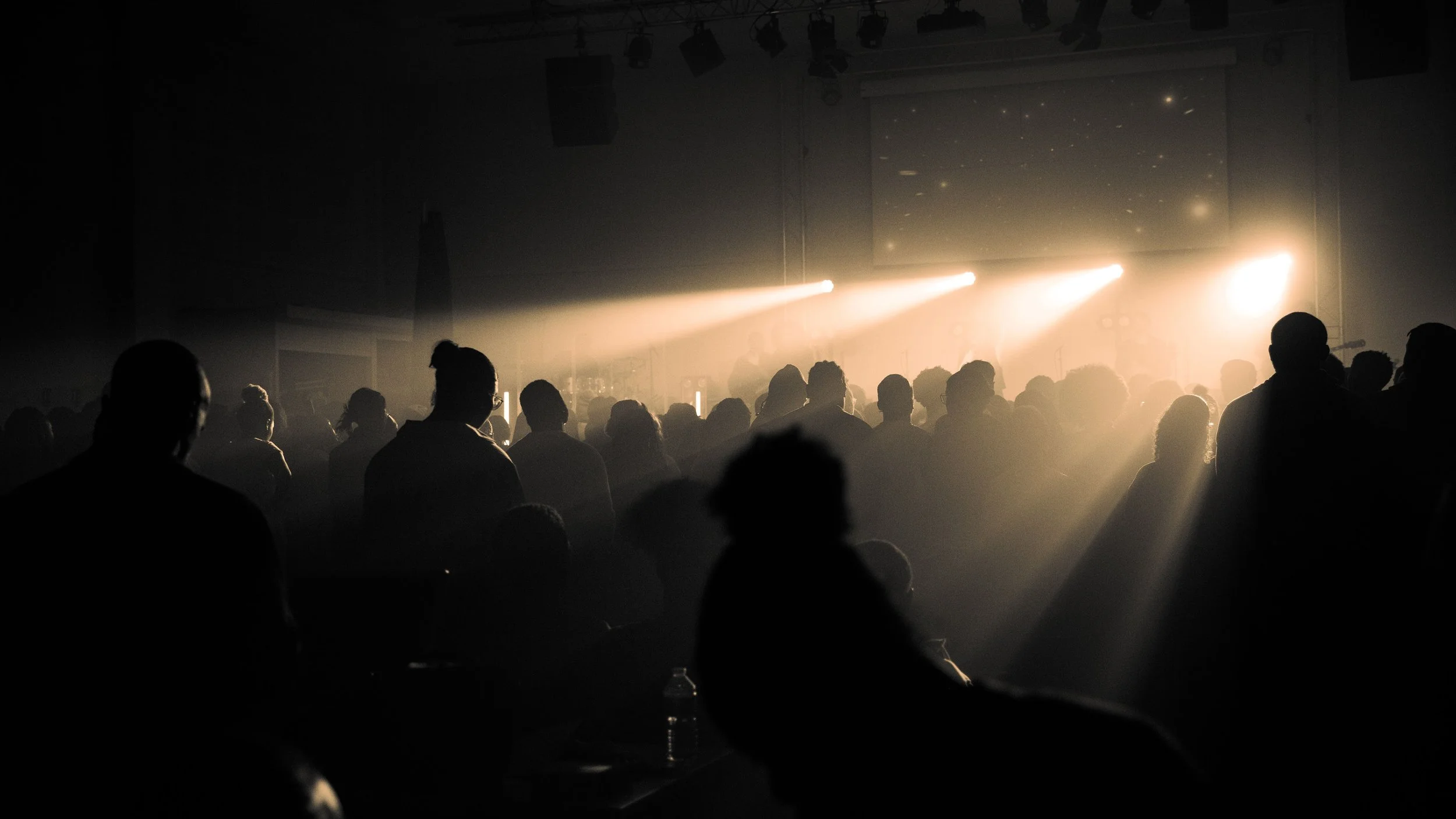 Une foule de personnes dans une salle sombre, illuminée par des lumières de scène, probablement lors d'un concert ou d'un événement en intérieur.